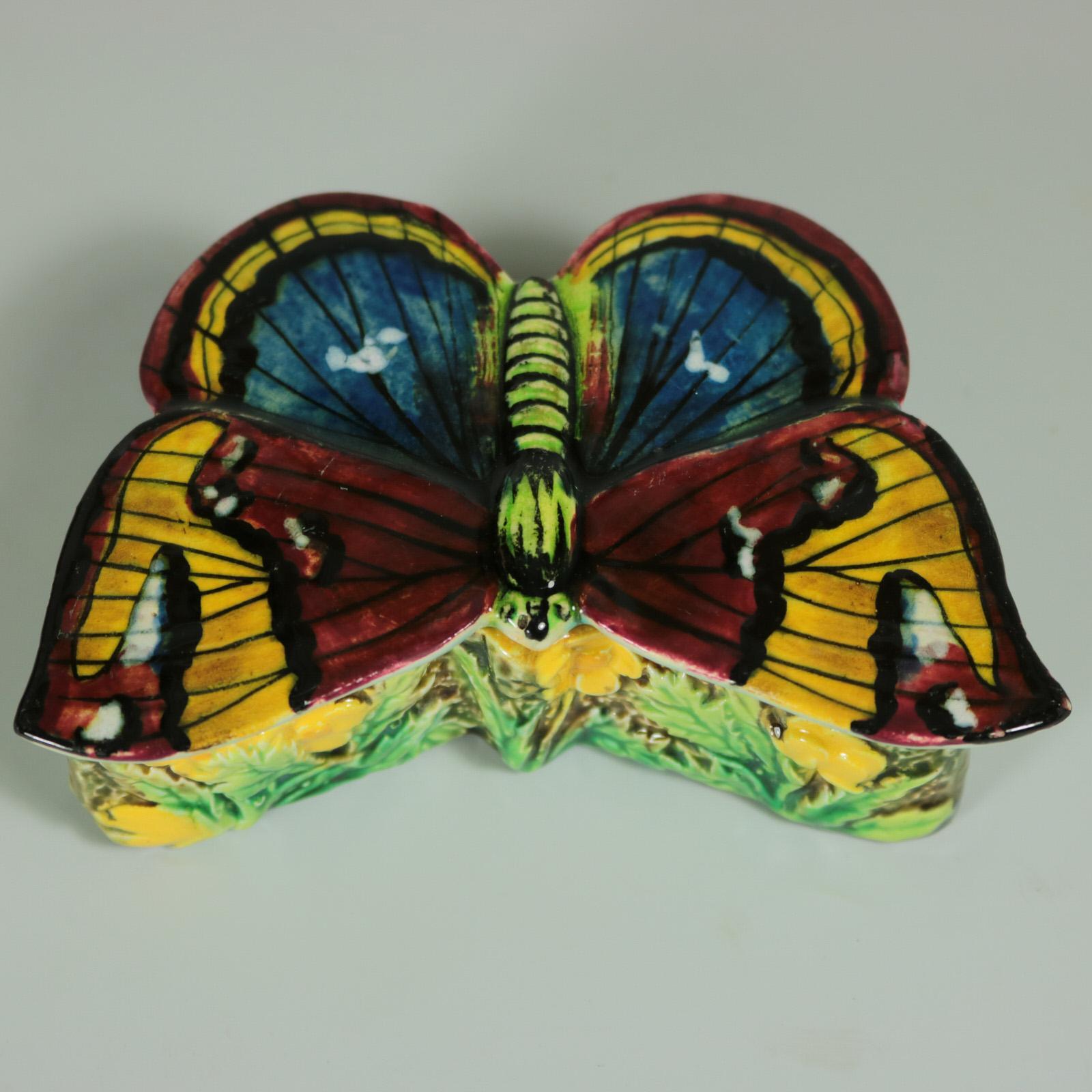 George Jones Majolica match box which features a butterfly forming the removable lid. The base is embellished with buttercups around the sides. Coloration: scarlet, yellow, blue, are predominant. English diamond registration mark for the date