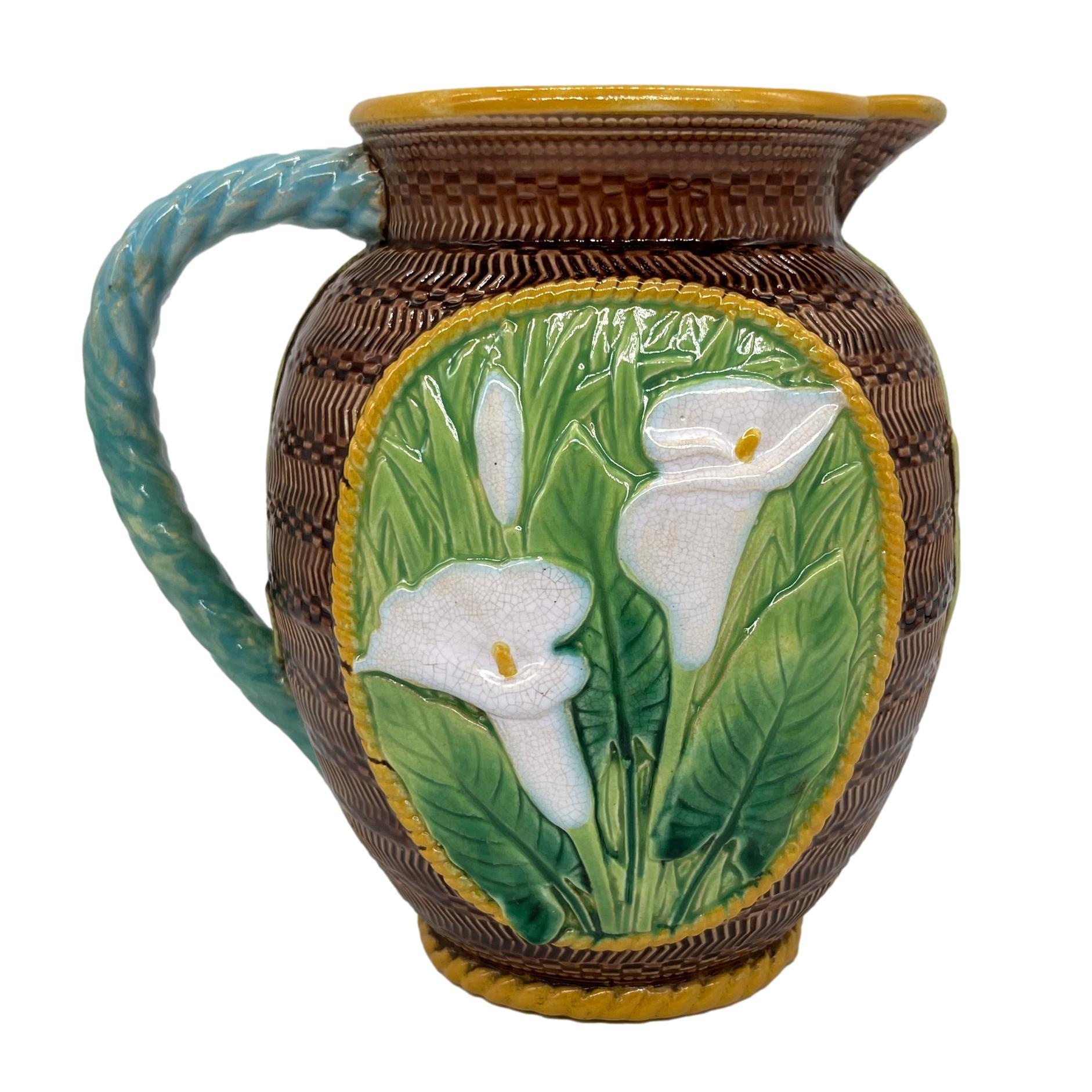 George Jones majolica pitcher with relief molded calla lilies and leaves in panels to either side, with yellow glazed cable borders and rope handle, the body decorated with engine-turned concentric, geometric bands and beading, the interior glazed