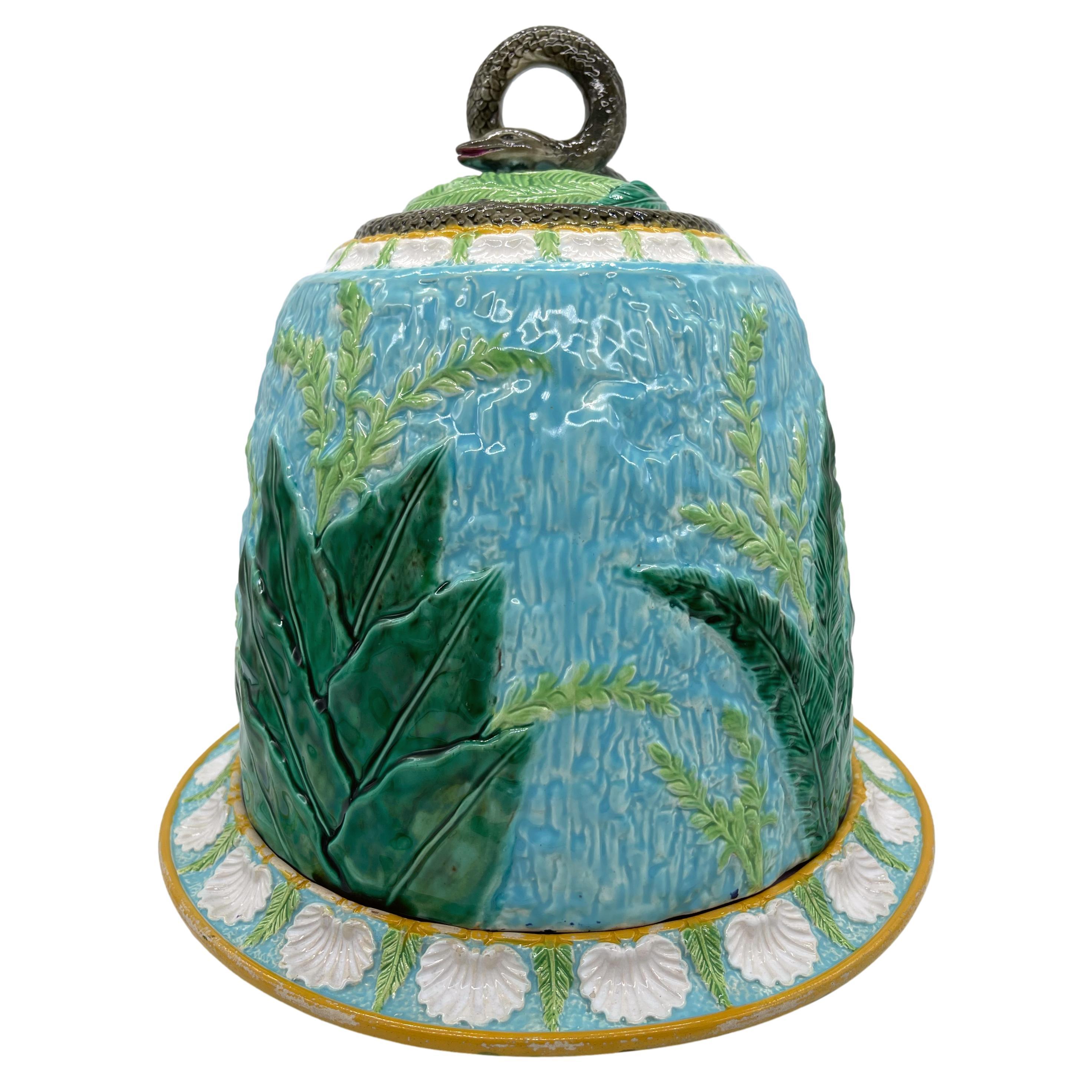 George Jones Majolica Cheese Bell and Stand, the dome with green-glazed leaves, ferns, and flowering grasses, on a bark-textured turquoise ground, the top banded with shells and acanthus leaves, a coiled, smiling snake among palms and ferns forming