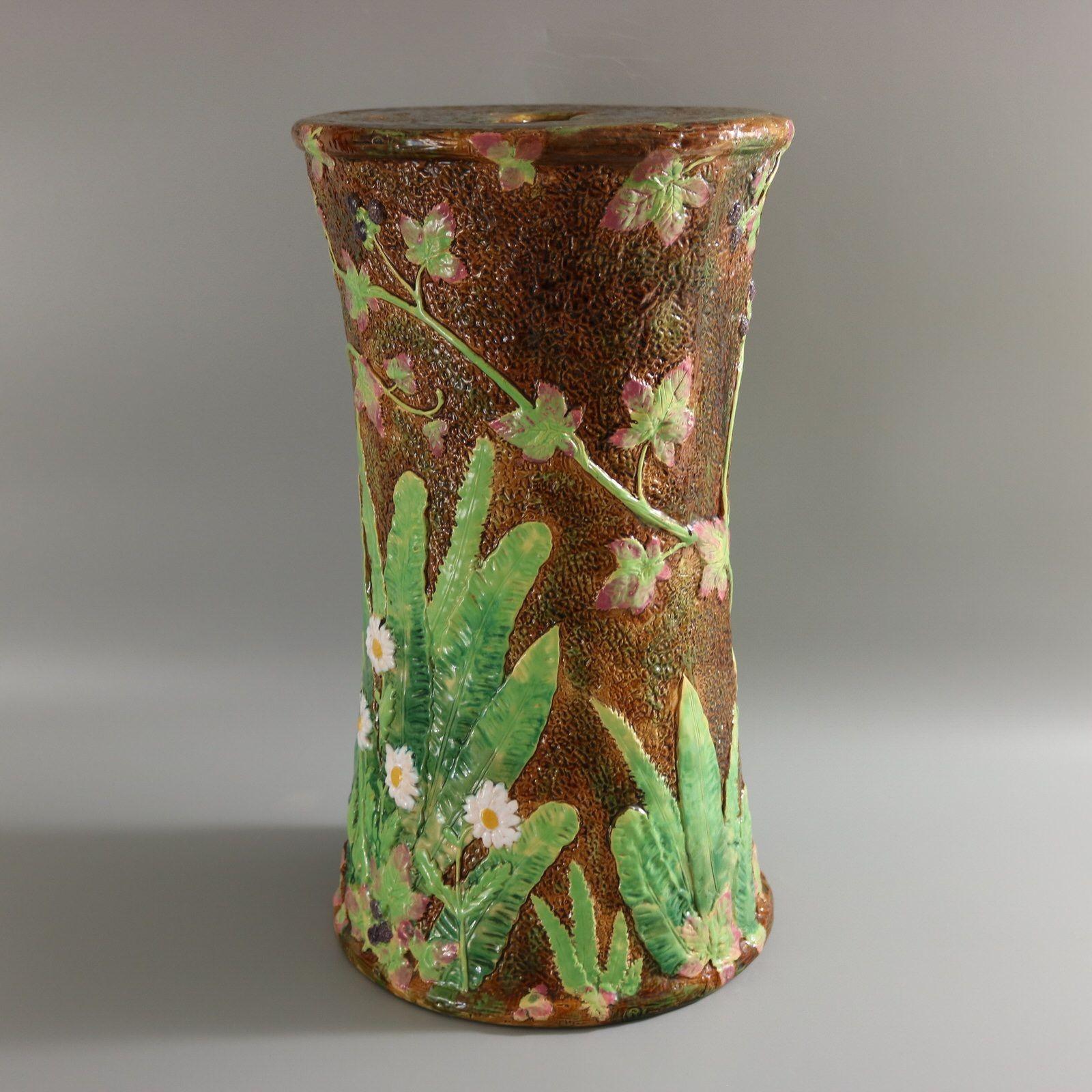 George Jones Majolica garden seat which features flowers (daisies) surrounded by leaves and foliage. Blackberries meandering around the sides. Colouration: brown, green, white, are predominant. The piece bears maker's marks for the George Jones
