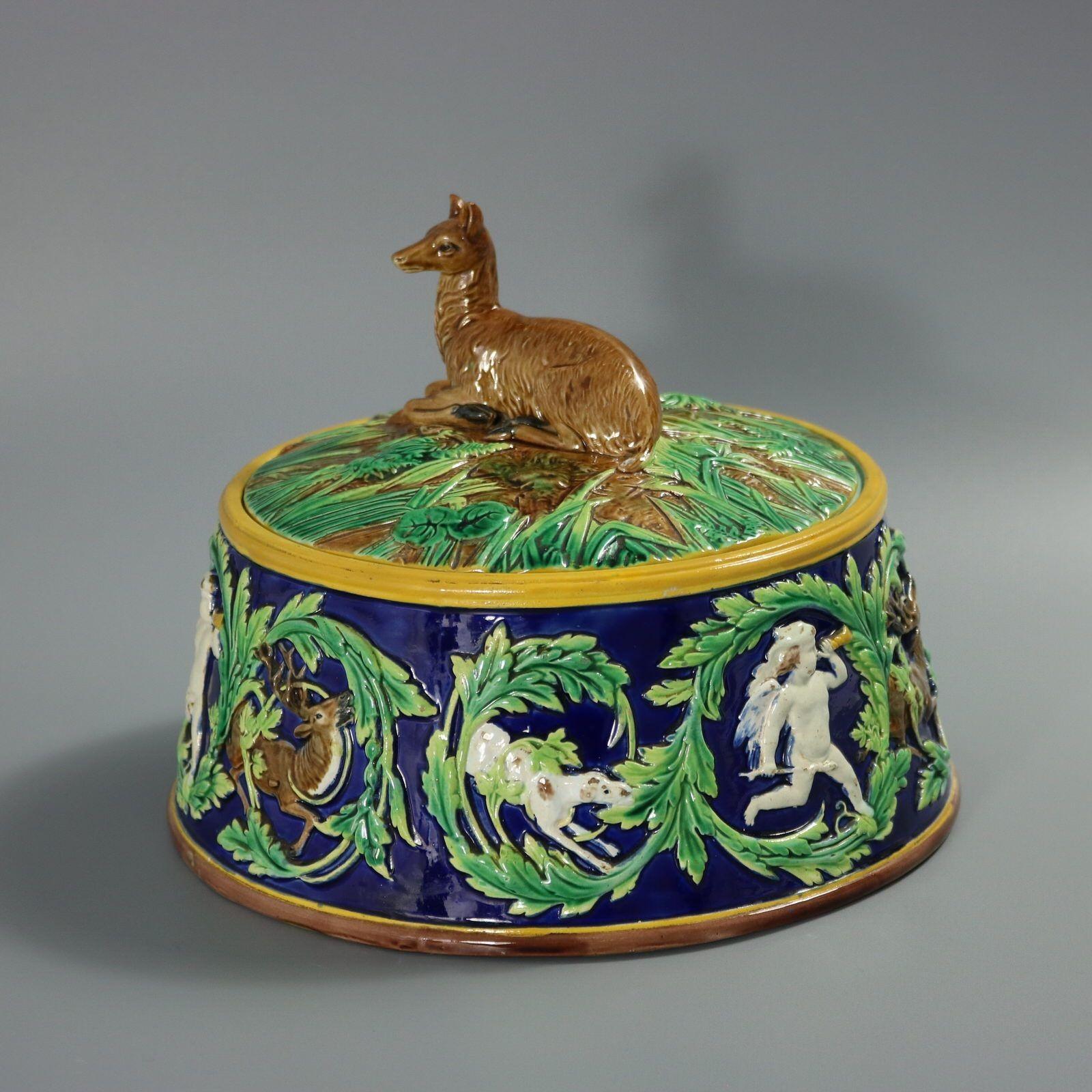 Plat à tarte à gibier en majolique de George Jones avec doublure qui présente un cerf couché (biche) formant l'anse, sur un fond feuillu. Le plat présente un motif répétitif de feuilles tourbillonnantes entourant un cerf, un chien et un chérubin