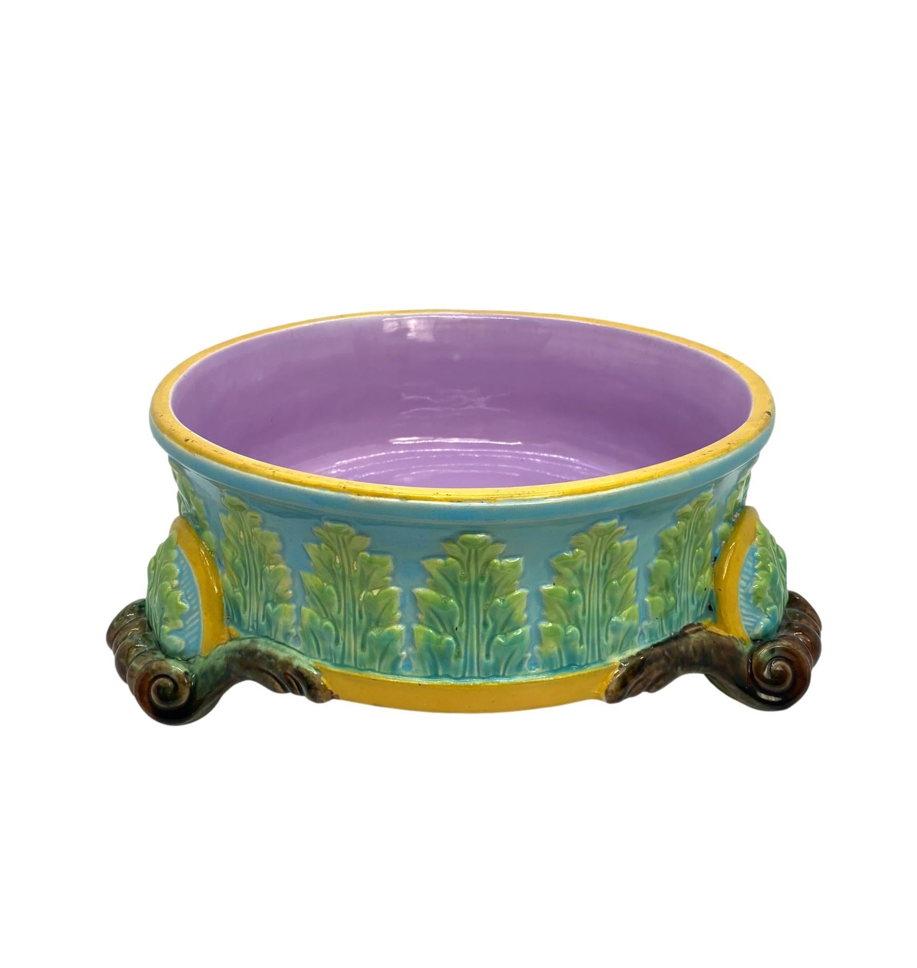 George Jones Majolica dog bowl, with green glazed acanthus leaves on a turquoise ground, bordered in ochre, with applied bowed cartouches above each of the scrolled feet, the interior glazed in pink, the reverse with impressed 'J' for 1884 and