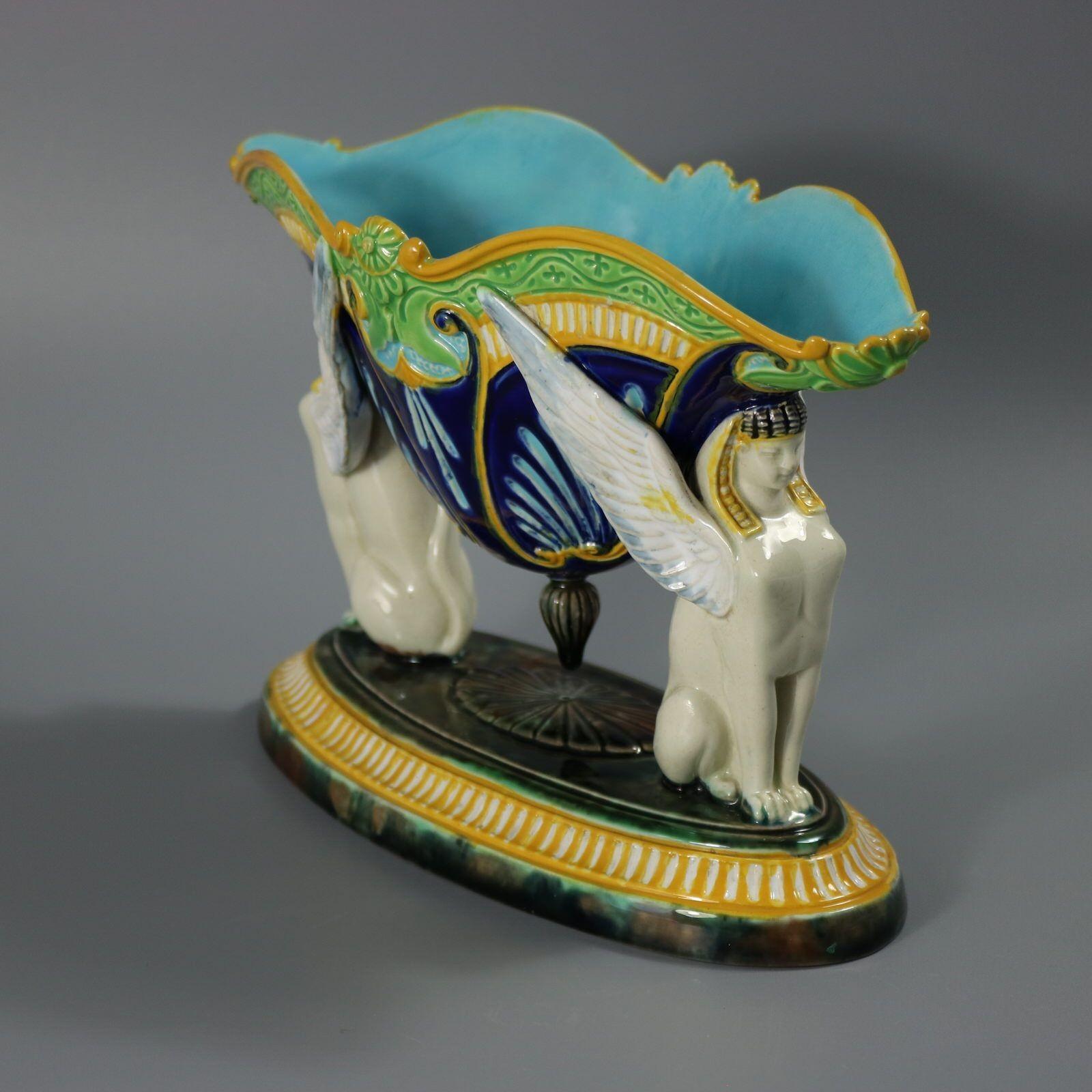 George Jones Majolica figural bowl with a mythological theme which features two Egyptian sphinxes seated on a mottled oval base supporting a bowl with their wings and their heads. Colouration: cobalt blue, ochre, white, are predominant. The piece