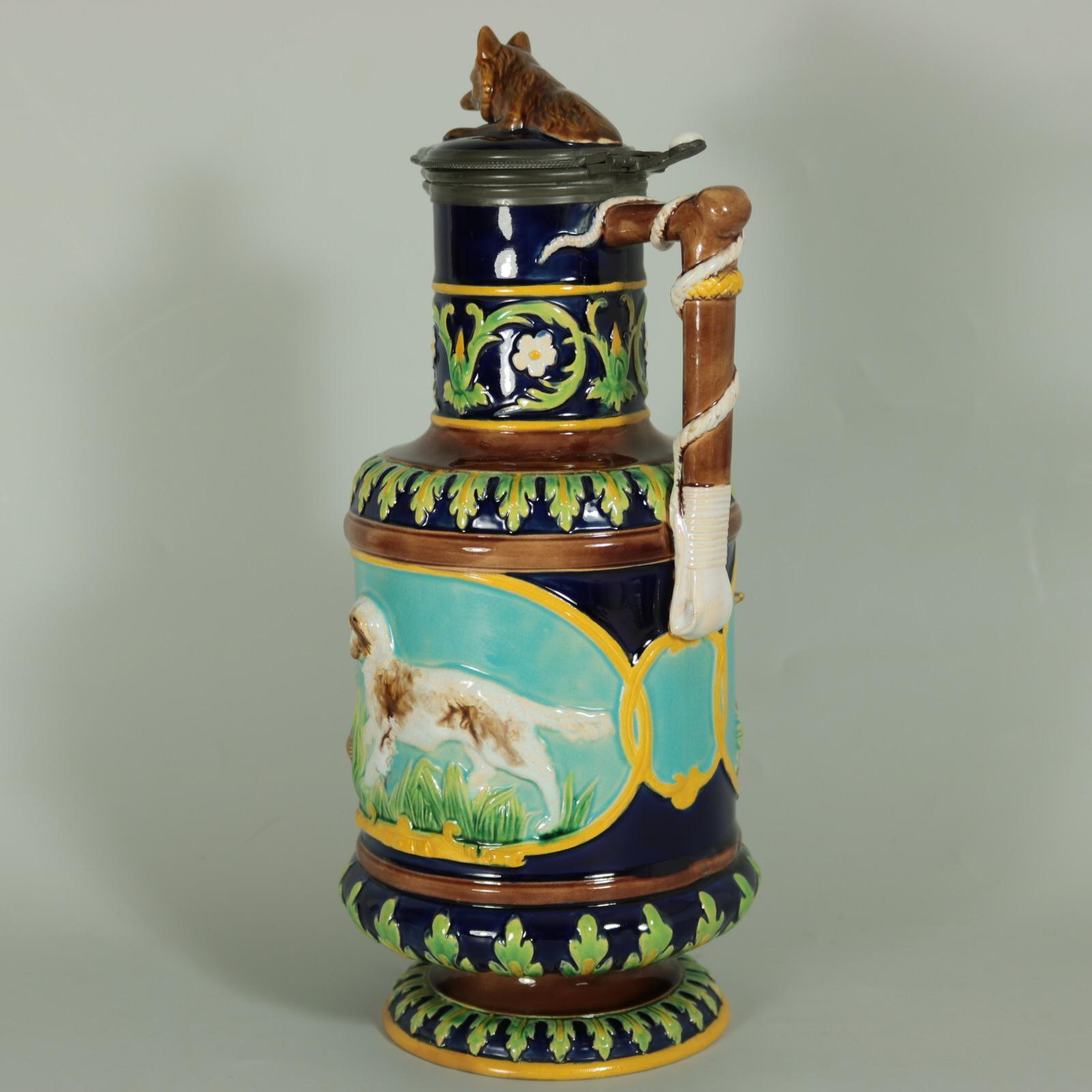 George Jones Majolica jug/pitcher with lid which features pictorial panels on either side, one depicts a retriever chasing a quail, the other a fox waiting to pounce on a rabbit. Colouration: cobalt blue, turquoise, green, are predominant. English