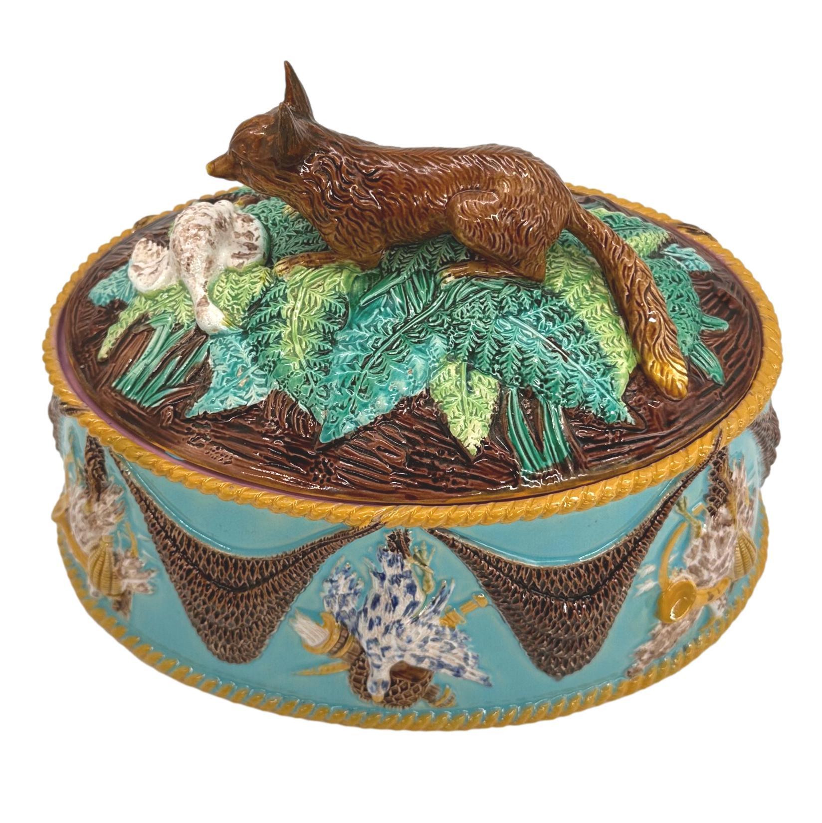George Jones Majolica Game Tureen, of oval form, the dish with alternating relief-molded game trophies and fishing net swags, bordered in yellow glazed roping, the cover with a domed rustic mound with green glazed ferns and grasses, surmounted by a