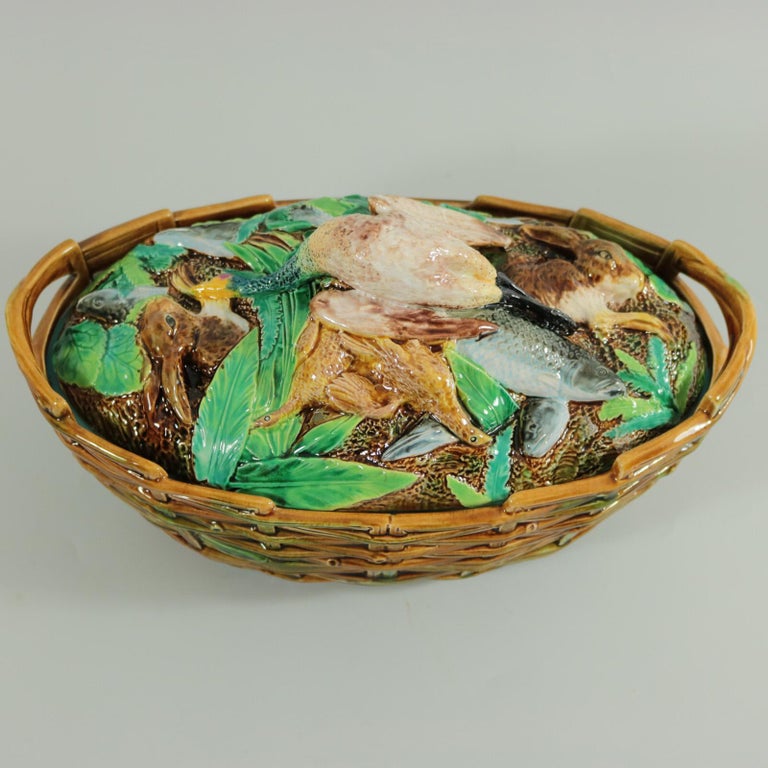 George Jones Majolica game pie dish with liner which features a goose, hares, birds and fish amongst leaves with a basket weave dish. Coloration: brown, green, white, are predominant. Bears a pattern number, '3569'. English diamond registration mark