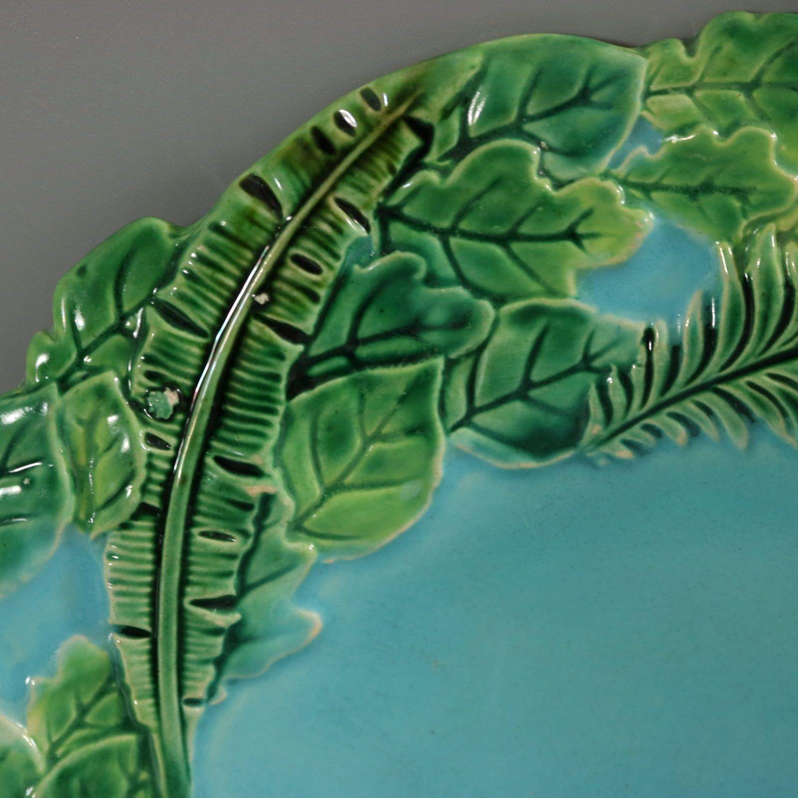 George Jones Majolica plate which features jungle plant leaves and ferns. Colouration: green and turquoise are predominant. Bears a pattern number, '3230'.