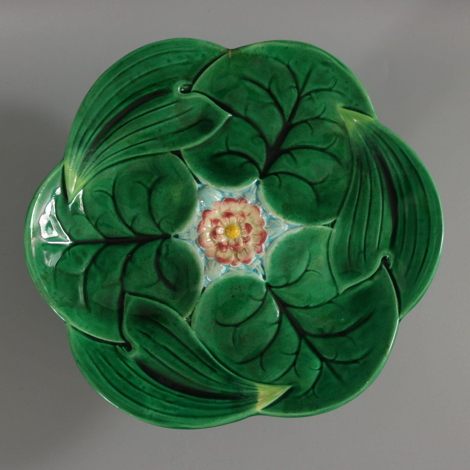 George Jones Majolica compote which features a pond lily flower surrounded by overlapping leaves. The pedestal modelled with leaves and a lily flower. Colouration: green, turquoise, pink, are predominant.