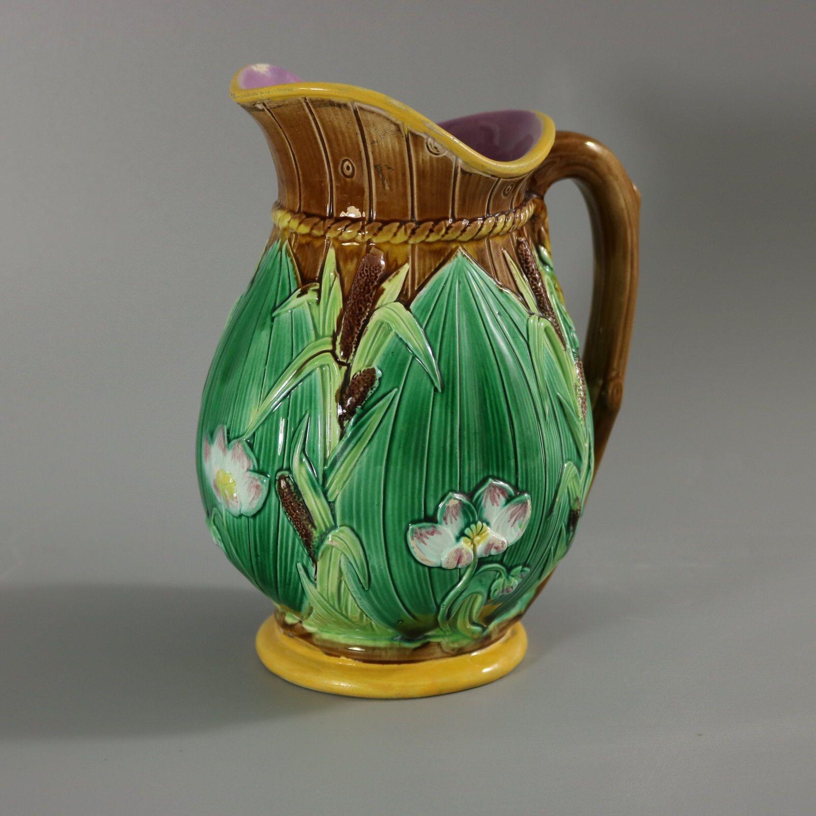 George Jones Majolica jug/pitcher which features lilies on a brown barrel ground. Colouration: brown, green, white, are predominant. Bears a pattern number, '1800'.