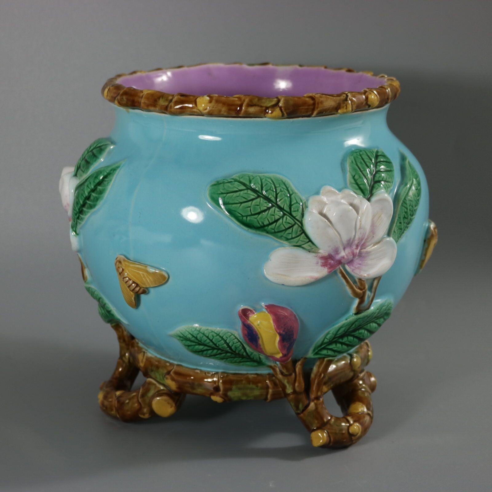 Cache-pot en majolique de George Jones représentant une fleur de magnolia et deux papillons de nuit. Version avec fond turquoise. Coloration : turquoise, vert, blanc, sont prédominants. Porte un numéro de modèle, 