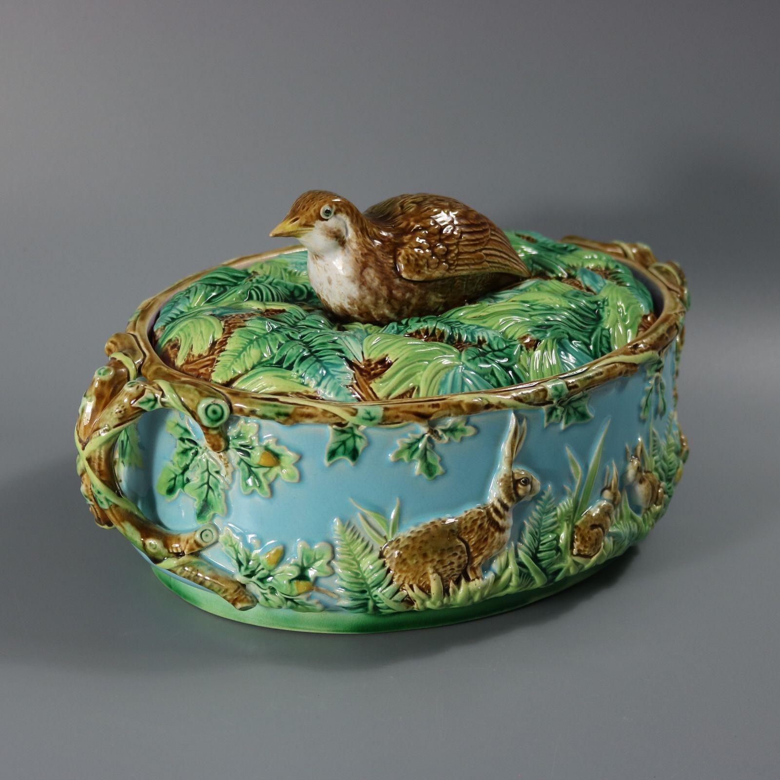 Plat à tarte à gibier en majolique de George Jones, dont le couvercle est orné d'un fleuron en forme de perdrix, assis au milieu de fougères et de feuilles. Les côtés du plat sont décorés de lapins et de feuilles. Poignées en branches de chêne à