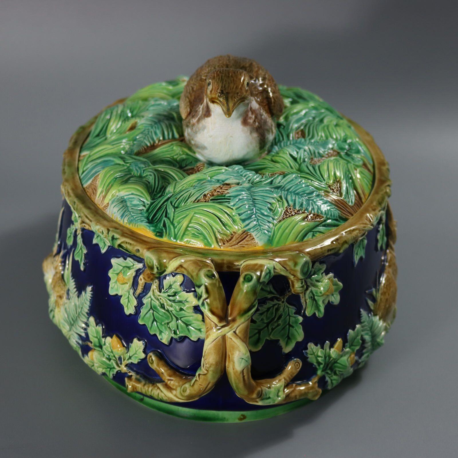 George Jones Majolica game pie dish which features a partridge finial on the lid, sitting amongst ferns and leaves. The sides of the dish decorated with rabbits and leaves. Oak branch handles to either end. Cobalt blue ground version. Colouration: