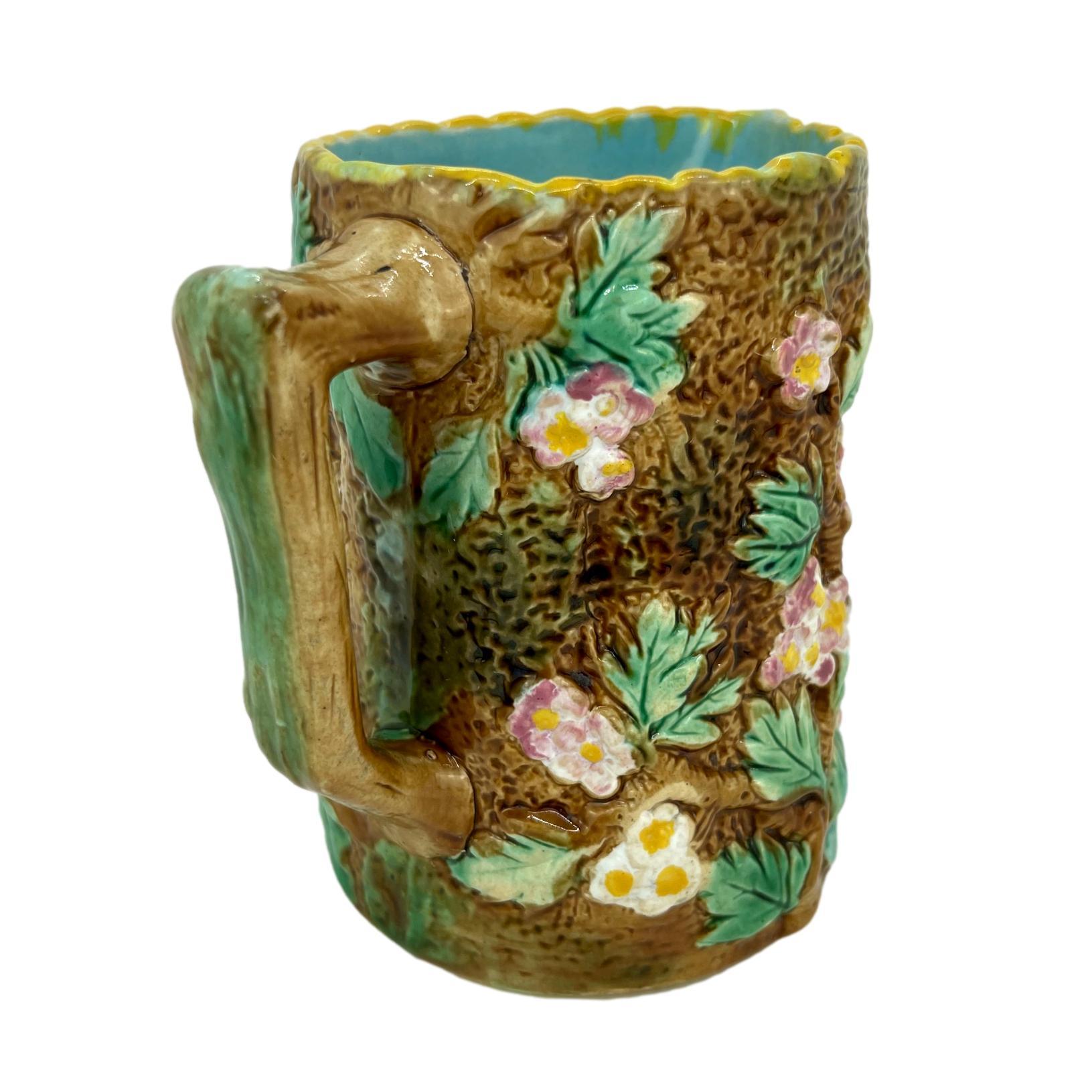 George Jones Majolica Pitcher, molded in high relief as a hawthorn tree, with branches, leaves, and pink blossoms on a mossy bark ground, the branch handle glazed in brown with green moss, the rim glazed in ochre, the reverse with painted design