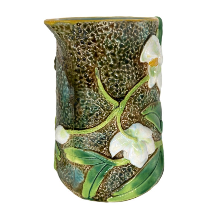 George Jones Majolica Pitcher, English, ca. 1875, with high relief-molded trompe l'oeil white orchids, with stems and leaves glazed in various shades of green, on a simulated mossy, watery bark ground, the handle formed by orchid leaves; the reverse