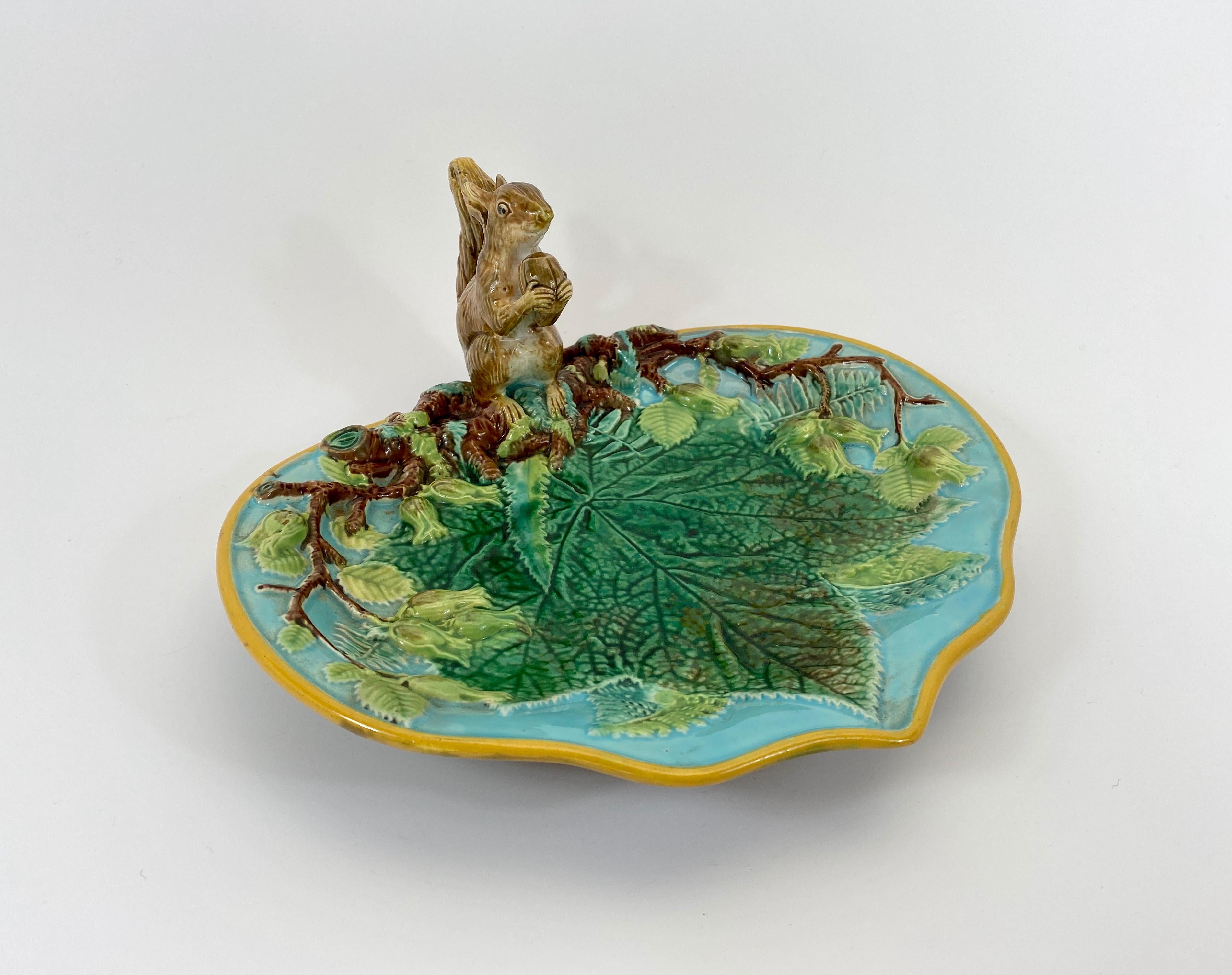 A George Jones Majolica squirrel dish, circa 1875. The dish, moulded in high relief, with a large leaf, and flowering branch. Surmounted by a finely moulded squirrel, holding a large nut. Covered in typical Majolica glazes.
The underside decorated