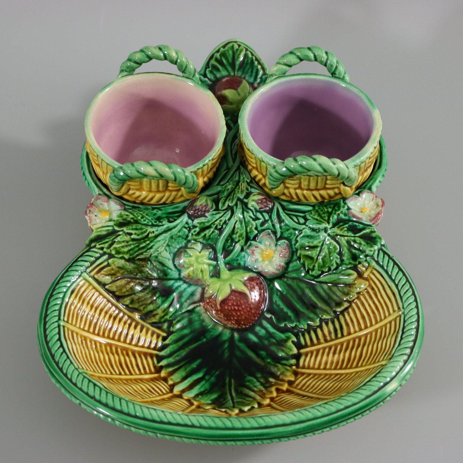 George Jones Majolica strawberry server, creamer & sugar which features a basket with two wells decorated with strawberries, leaves and blossom. Removable cream and sugar bowls in the form of baskets. Colouration: yellow, green, red, are