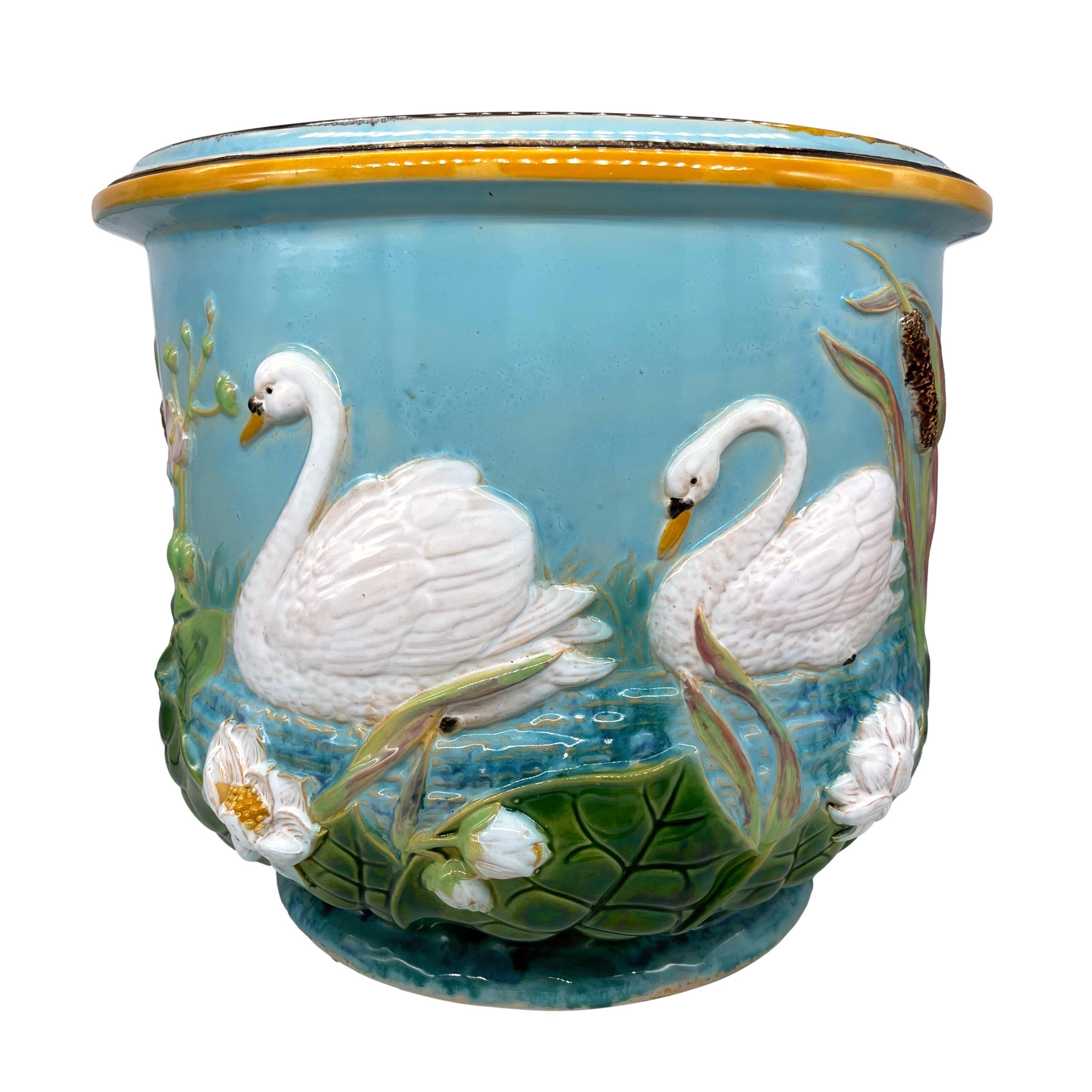 George Jones majolica jardinière, the cylindrical body with relief-molded white swans, waterlilies, pads, and cattails on simulated water with reeds to the background, on a turquoise ground, the interior glazed in lilac, the reverse with