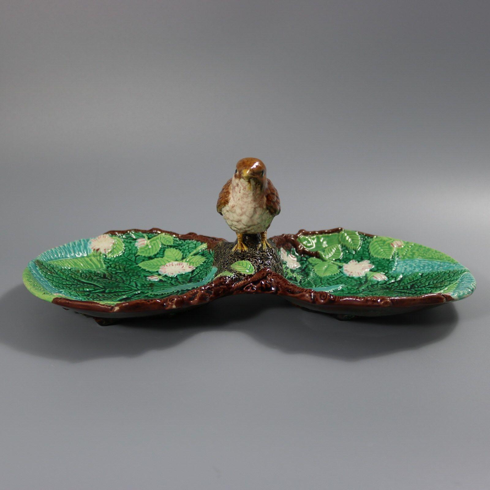 Plat en majolique de George Jones dont l'anse est formée d'un oiseau (grive). Deux lobes de chaque côté avec de la fougère, des fleurs et des feuilles d'érable. Coloration : le vert, le brun et le blanc sont prédominants. Porte un numéro de modèle,