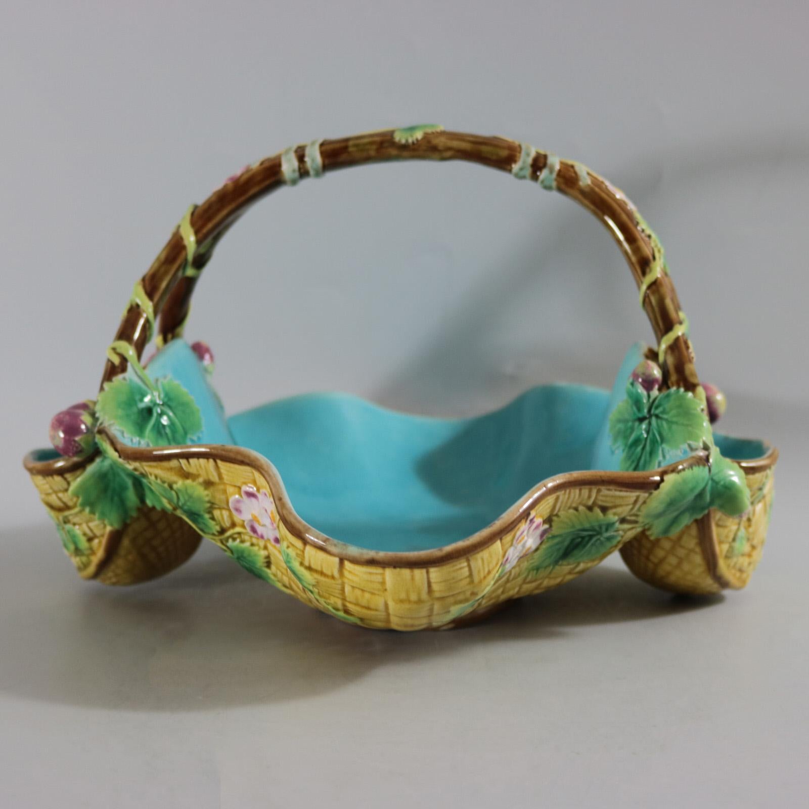 George Jones Majolica basket which features yellow woven basket sides and a branch handle. Embellished all over with strawberry leaves, flowers and fruit. Colouration: turquoise, yellow, green, are predominant. Bears a pattern number, '5276'.