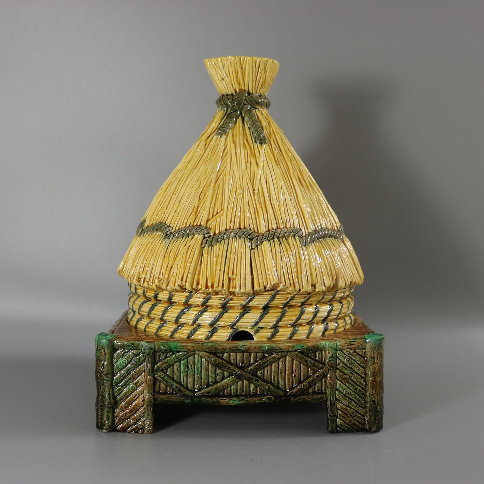 George Jones Majolica cheese keep which features a straw thatched beehive, bound with rope. The base in the form of a wooden platform. Yellow ground version. Colouration: yellow, brown, green, are predominant. Bears a pattern number, '3249'. English