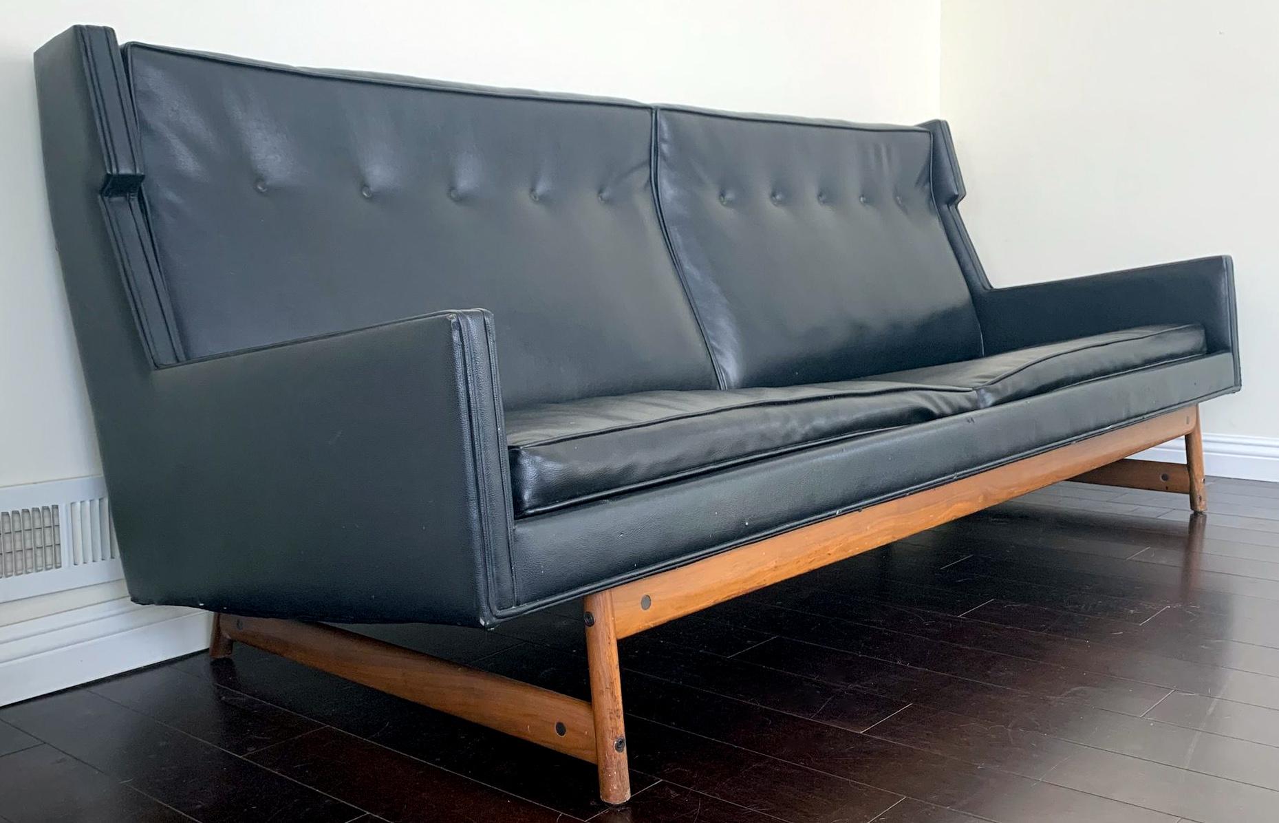 Available right now we have this absolutely stunning George Kasperian wingback sofa. This 1970s sculptural sofa features a black weathered leather upholstery with a gorgeous natural walnut splayed leg frame so beautiful it would be a crime to hide