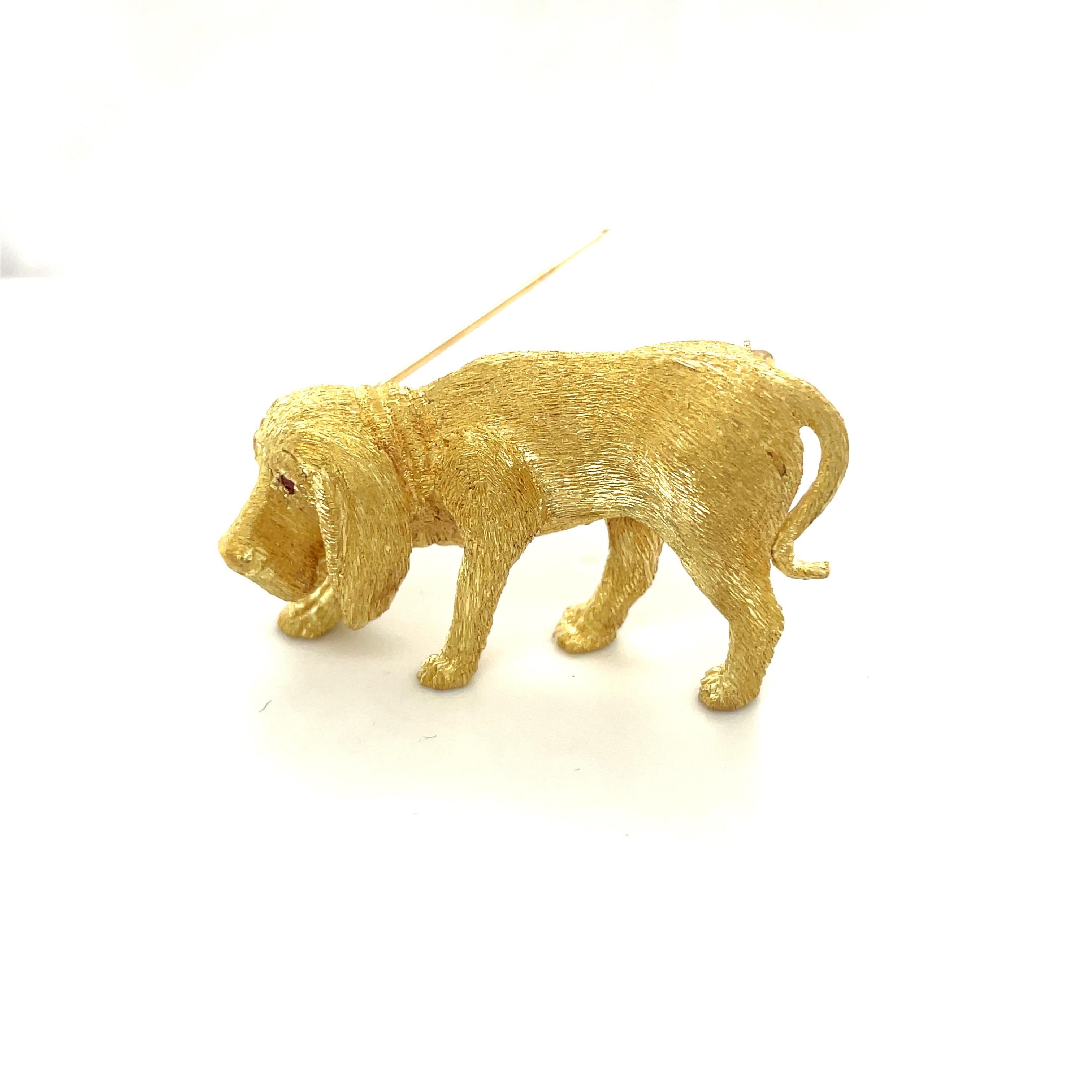 This 18 karat yellow gold Bloodhound brooch is crafted in an etched satin finish. The pup's eyes are set with round brilliant rubies. The brooch measures 1-3/4