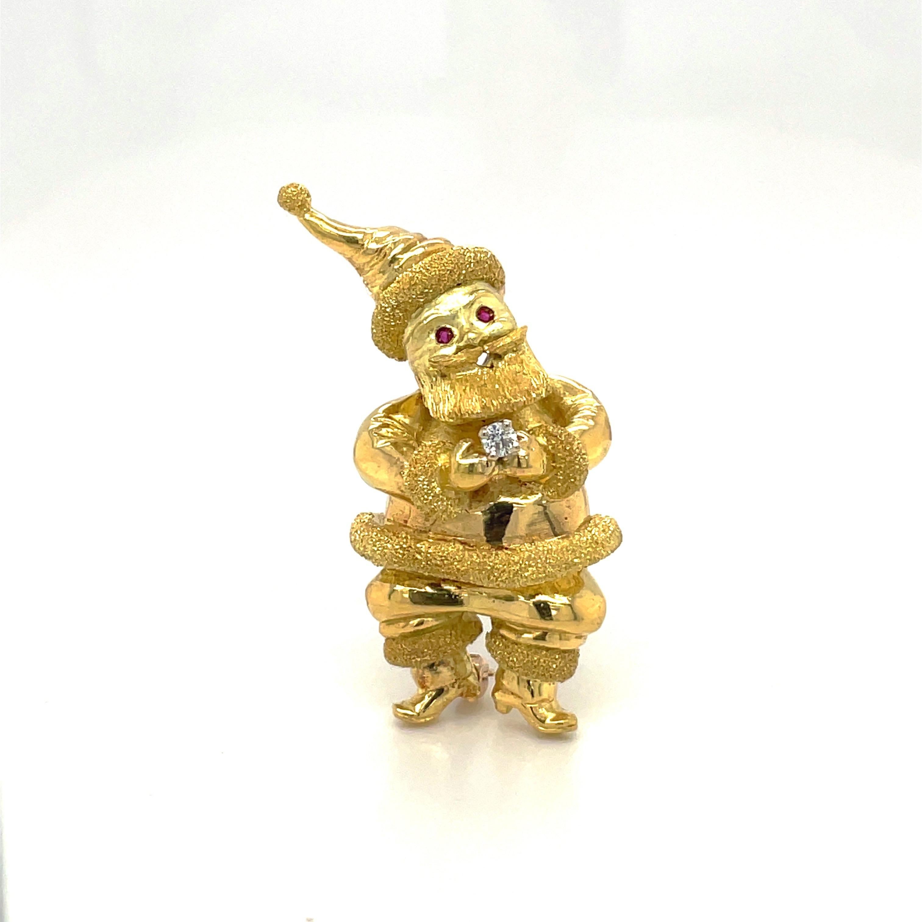 A jolly 18 karat yellow gold Santa Claus brooch. The brooch is designed with mixed finishes of sand blasting and high polish giving Santa Claus lovely depth. He has ruby eyes and holds a single round diamond in his hands. The brooch measures 1.5