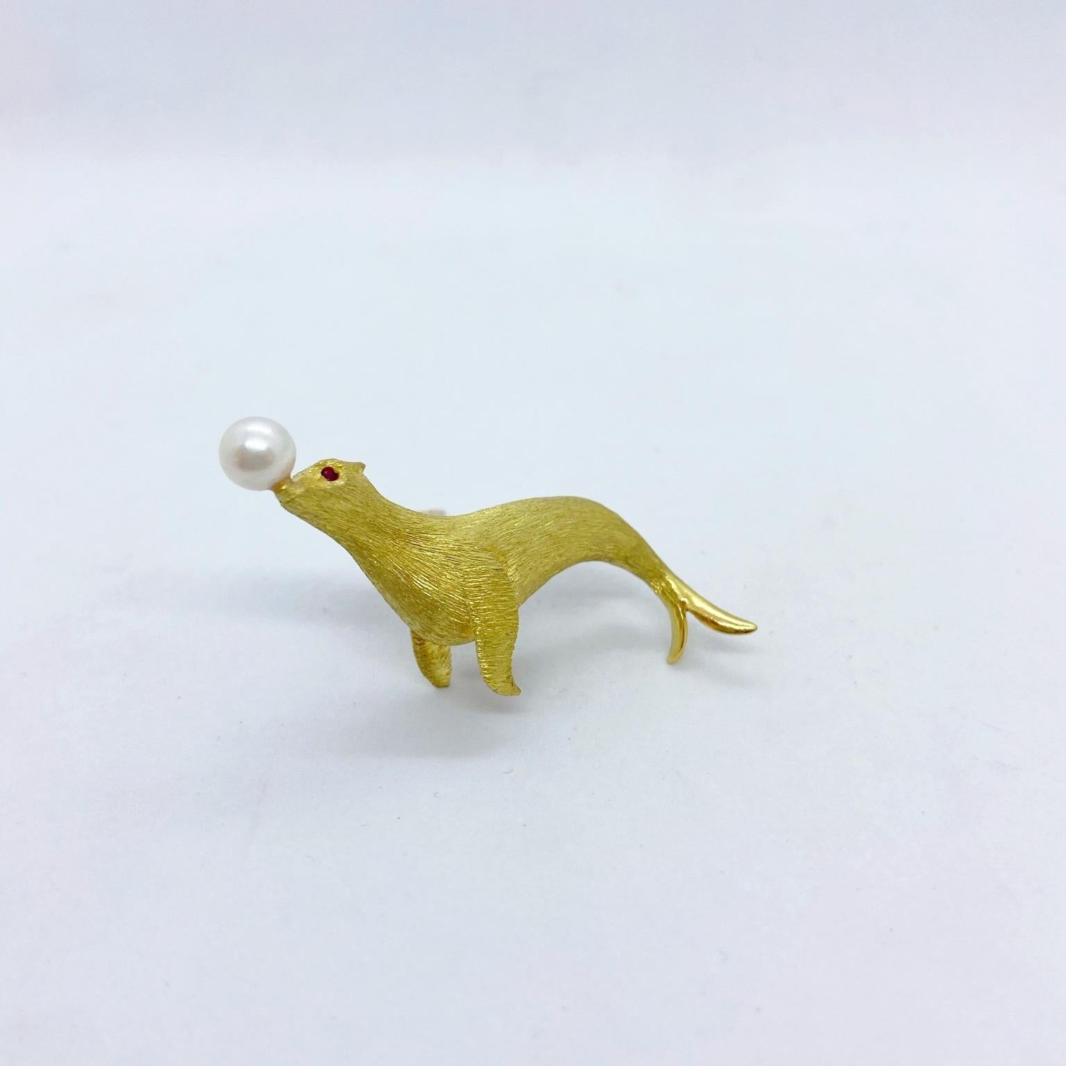 This 18 karat yellow gold brooch is designed as an adorable seal balancing a pearl ball on his nose. the brooch is in a sandblasted finish with ruby eyes. The brooch measures 2