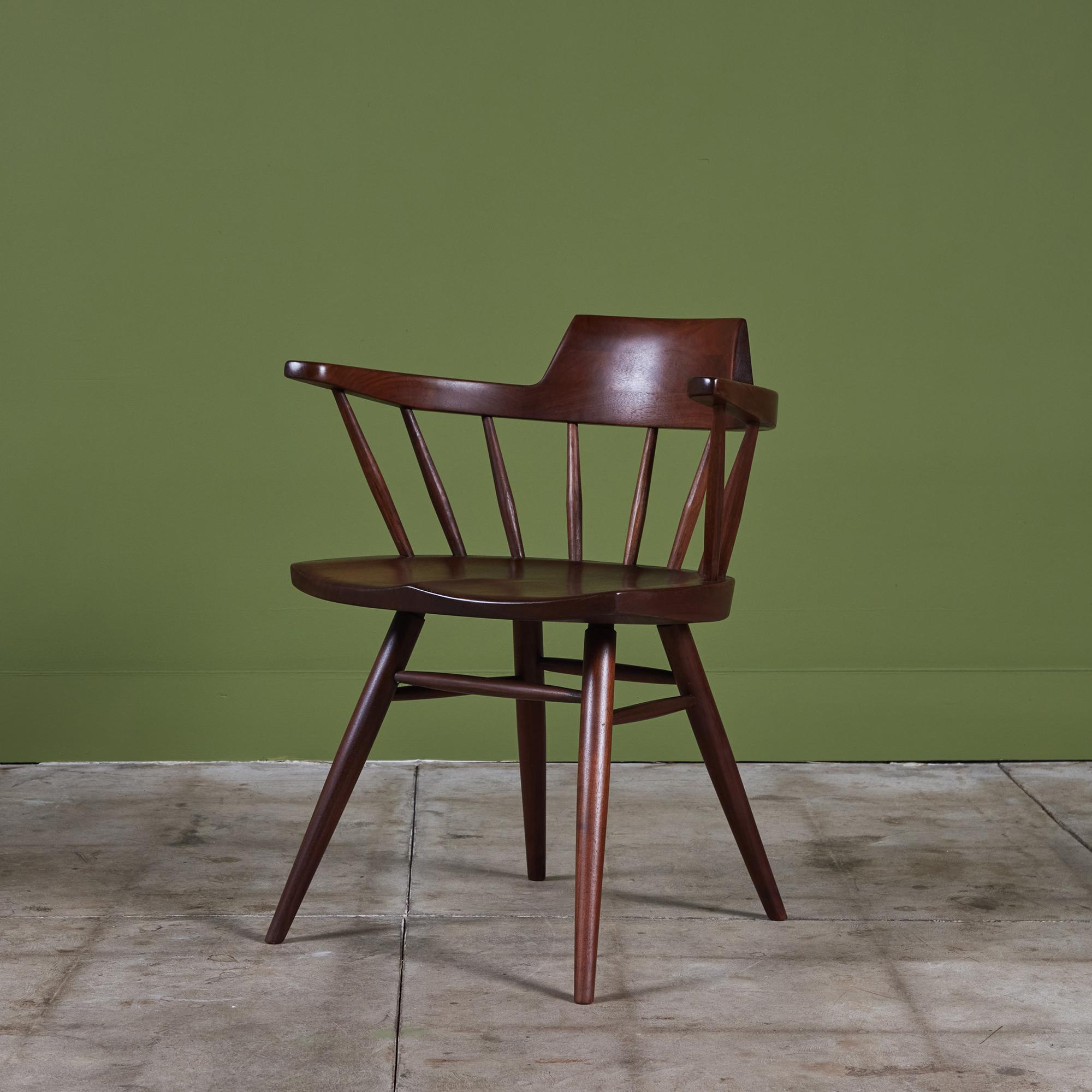 Fauteuil capitaine de l'artisan américain du milieu du siècle George Nakashima. La chaise en noyer noir est dotée d'un dossier incurvé, surmonté de fuseaux sculptés, inspiré de la chaise Windsor et des pièces Shakers. L'assise est sculptée à la main