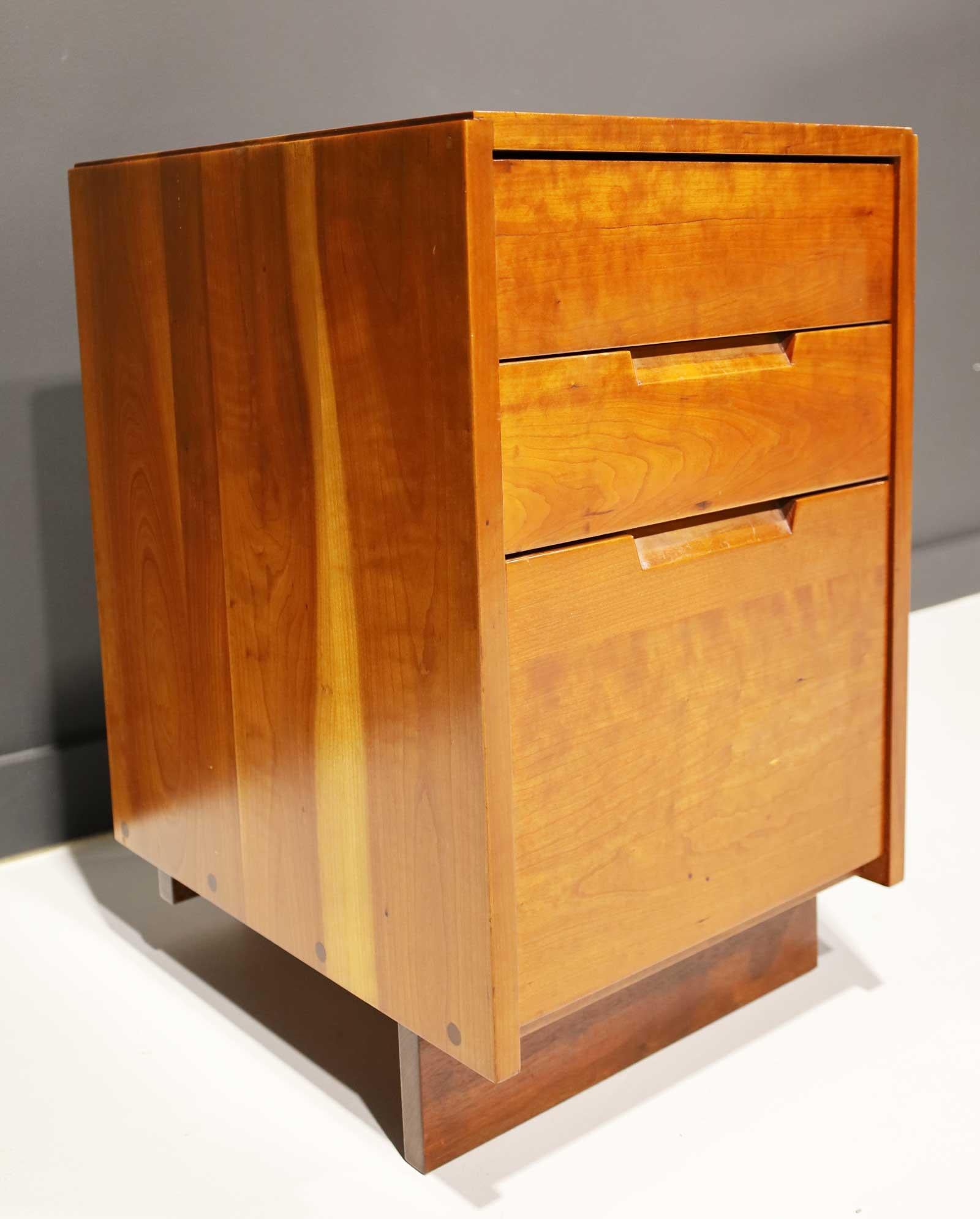 George Nakashima cherry nightstand or pedestal side table with sub sap streak on top and sides. The nightstand has three drawers and a toe base. All original paperwork and certificates of authenticity available.