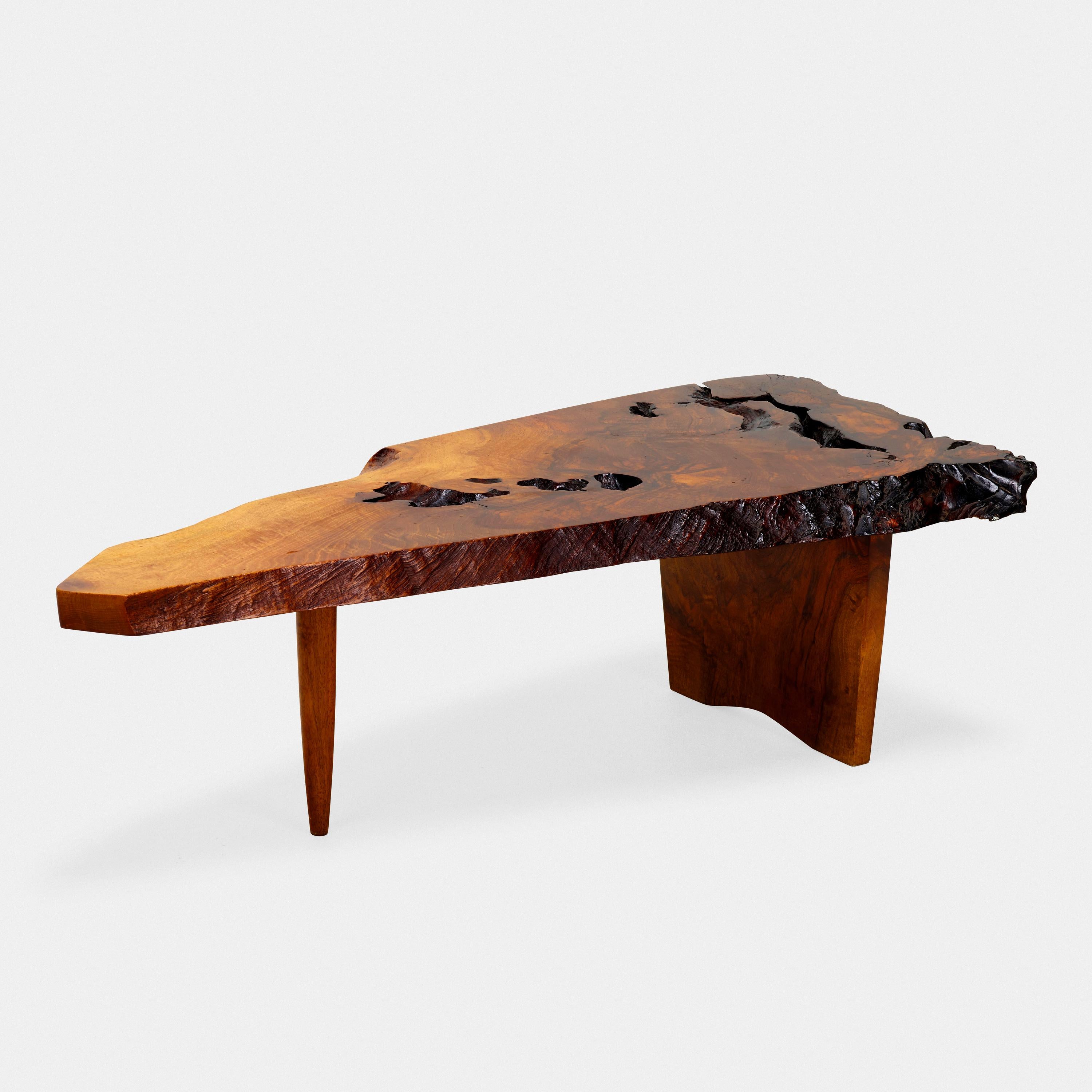 An exquisite George Nakashima Conoid cocktail table executed in English walnut, its subtriangular, slab top with three live edges, and featuring expressive grain / details, naturally occurring separations, and open knots. Underside bears client's