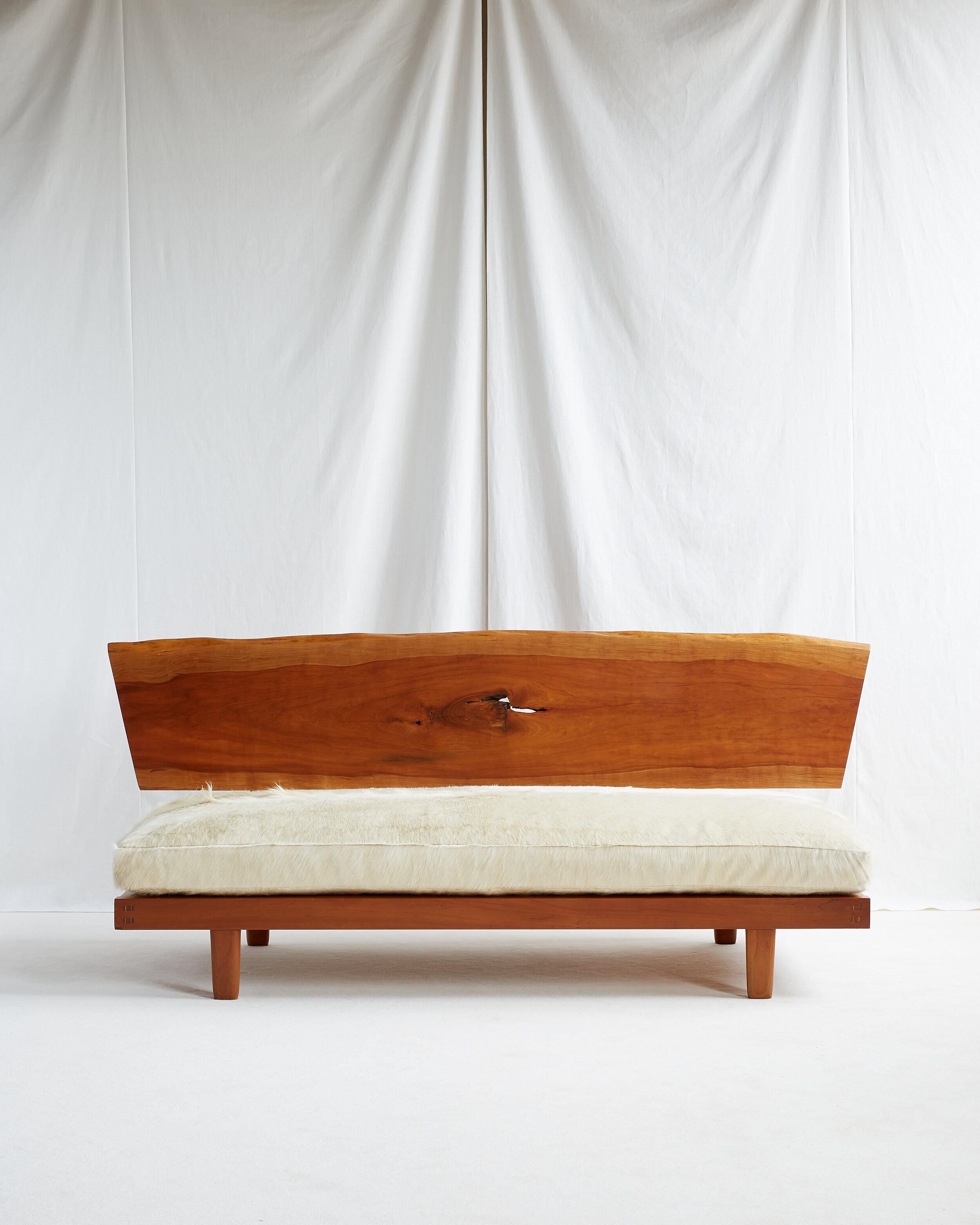 Beautiful freeform single board cherry slab back with sap grain and one central knot. 

Solid cherry frame with ovoid legs. Seat cushion upholstered with ivory Brazilian long hair cow hide, feather and down wrapped over foam. 

American c. 1964.