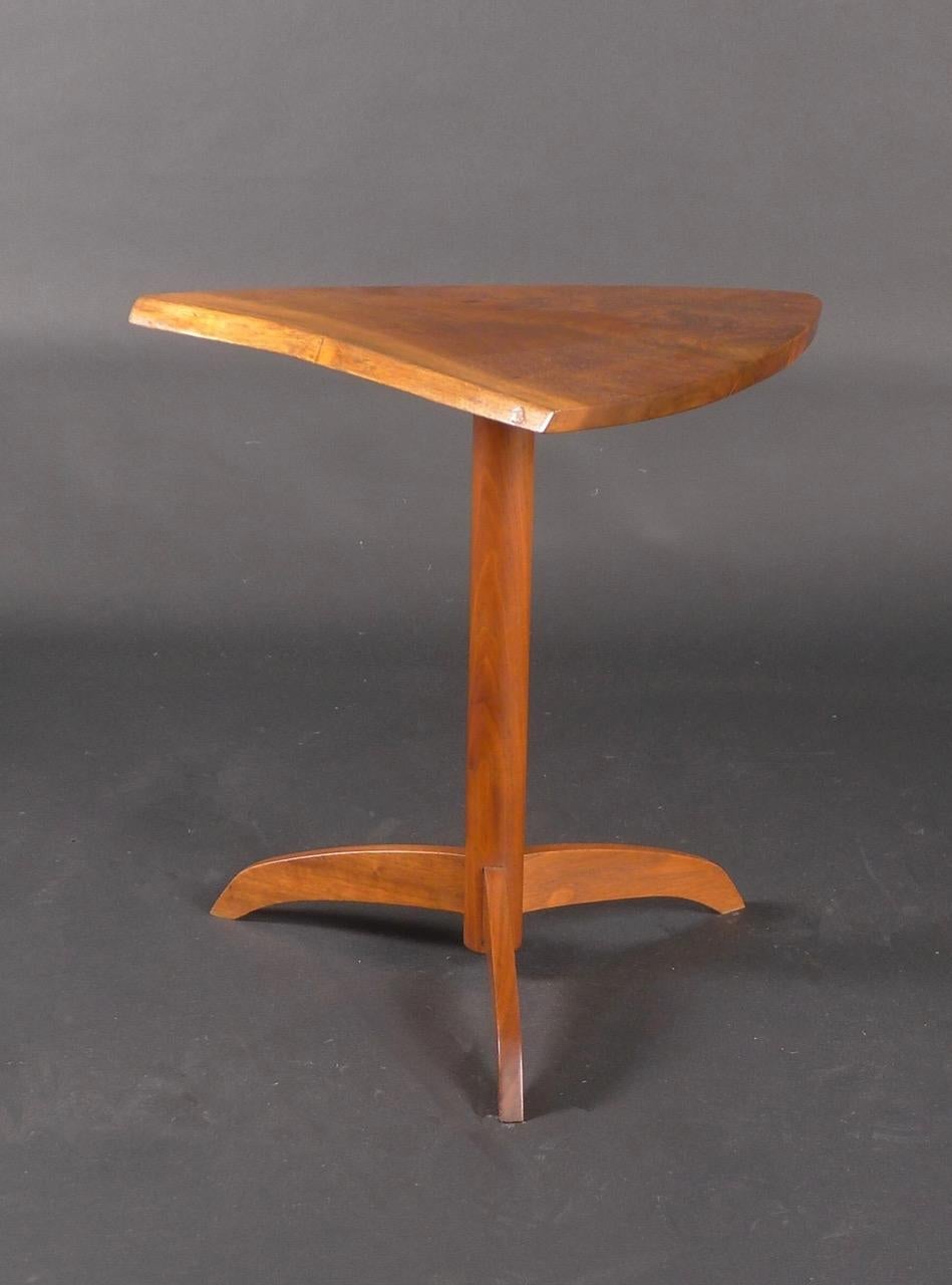 American black walnut pedestal end table, designed by George Nakashima and created in the George Nakashima studio at New Hope, Pennsylvania, US.  Irregular triangle top showcasing the beautiful grain of the wood, on column support and curved tripod