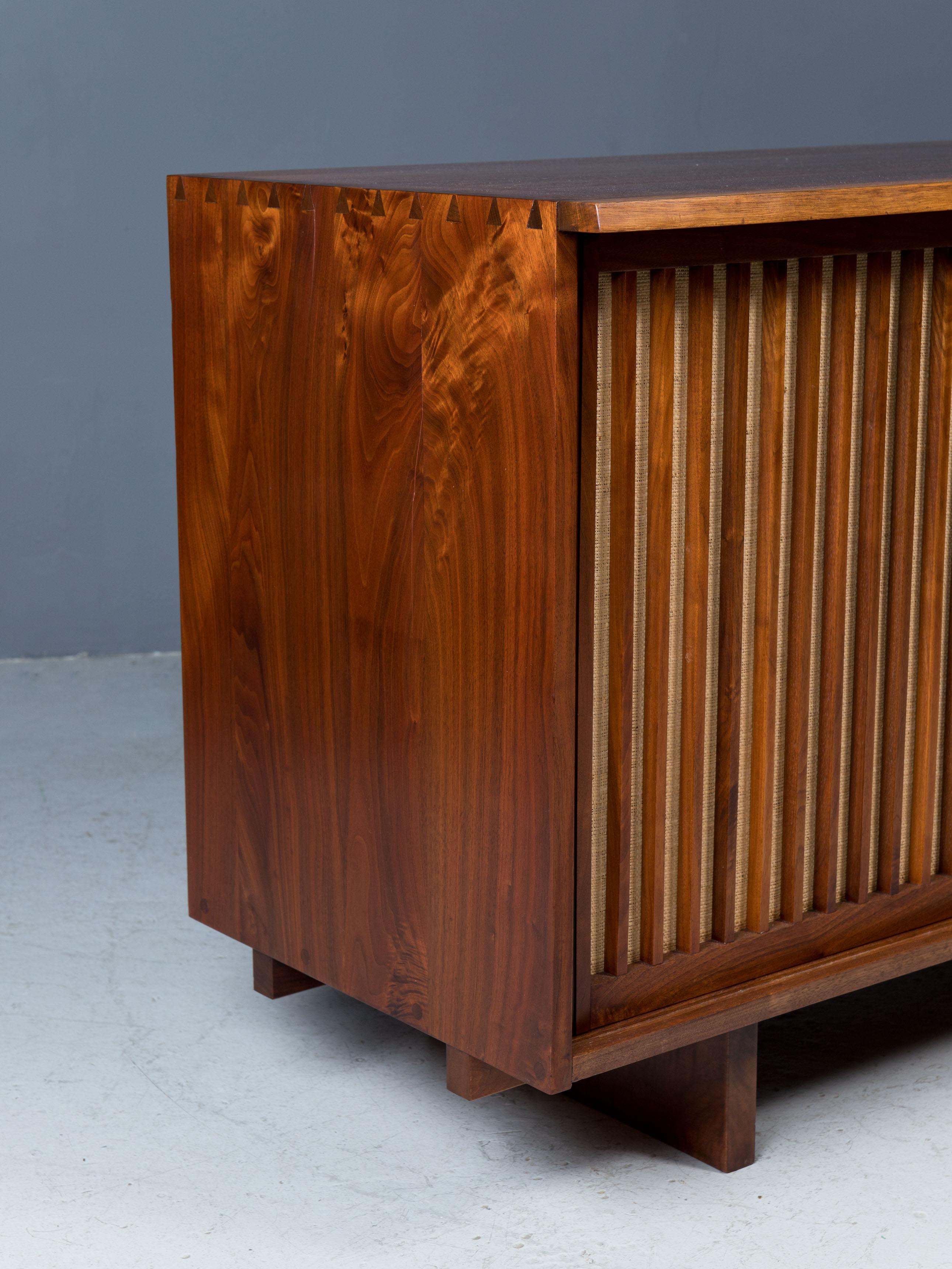 Cabinet features expressive American black walnut top with overhang
and free edge, two sliding doors concealing two adjustable shelves and
four drawers. 

Pandanus cloth is original.

Signed with client name on the back.

Sold with a digital