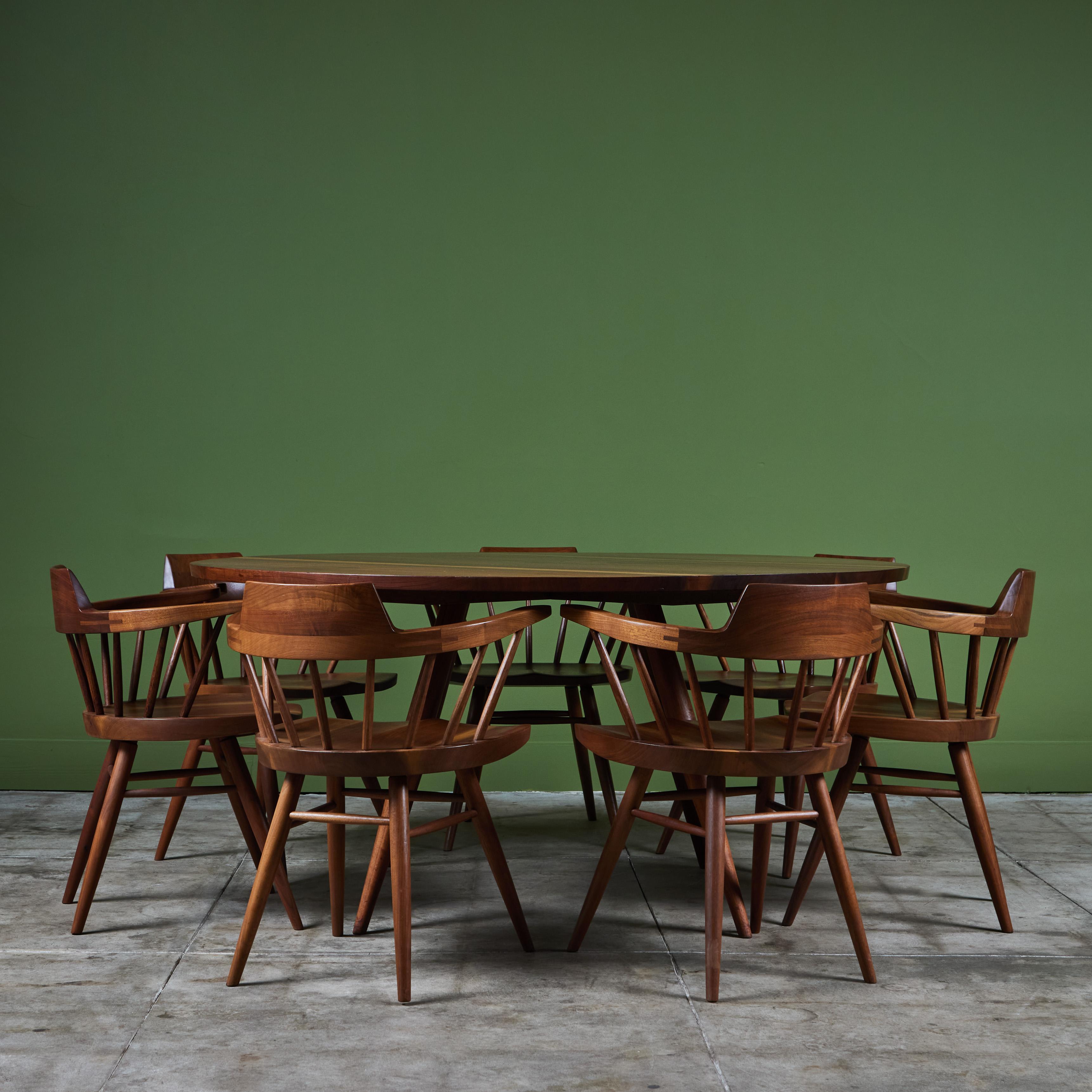 Dining set from American midcentury craftsman George Nakashima. The set features a large round black walnut dining table with four splayed tapered dowel legs The table top showcases book matched black walnut slabs with striking contrasting sap wood