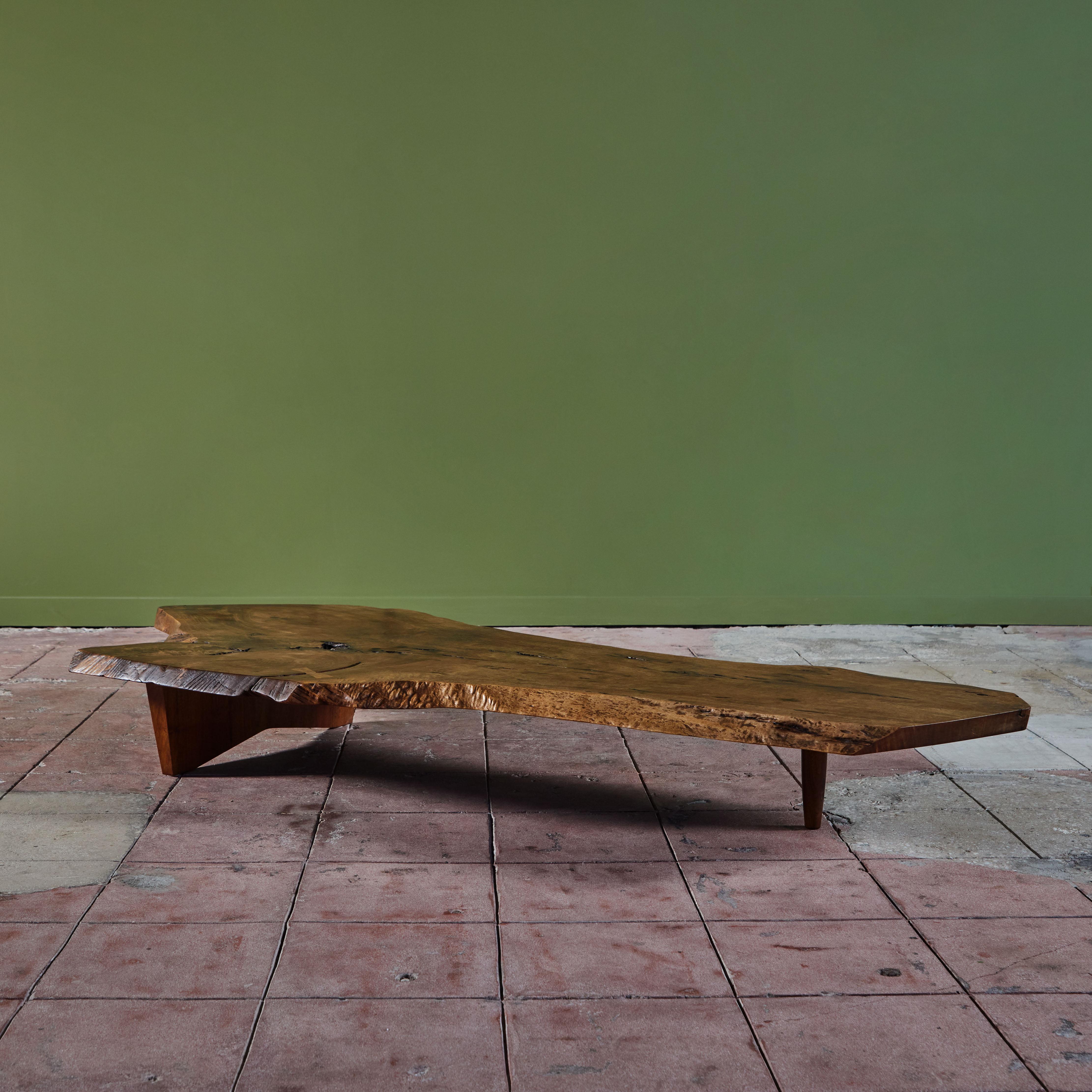Coffee table from American mid-century craftsman George Nakashima. The table crafted of black walnut, c.1969 features a live edge table top geometric slab base with one tapered leg. Purchased from the original owners and verified by the Nakashima