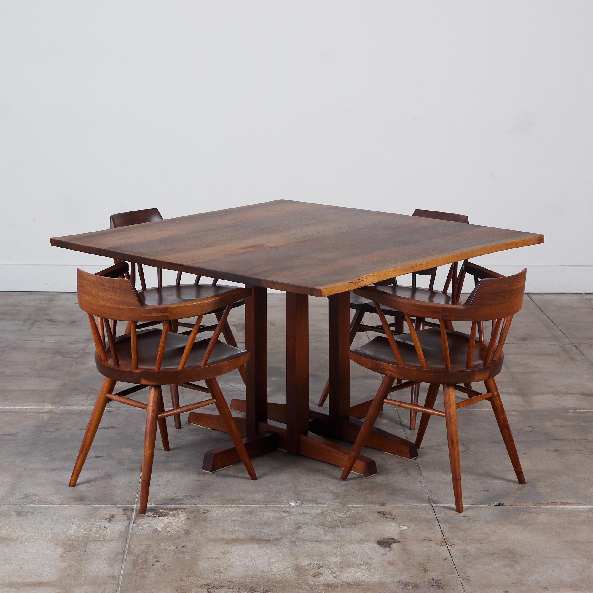 Dining set from American midcentury craftsman George Nakashima. The set features four black walnut captains chairs and square live edge dining table. The chairs, produced circa 1974 have curved, peaked backrests atop carved spindles, inspired by the