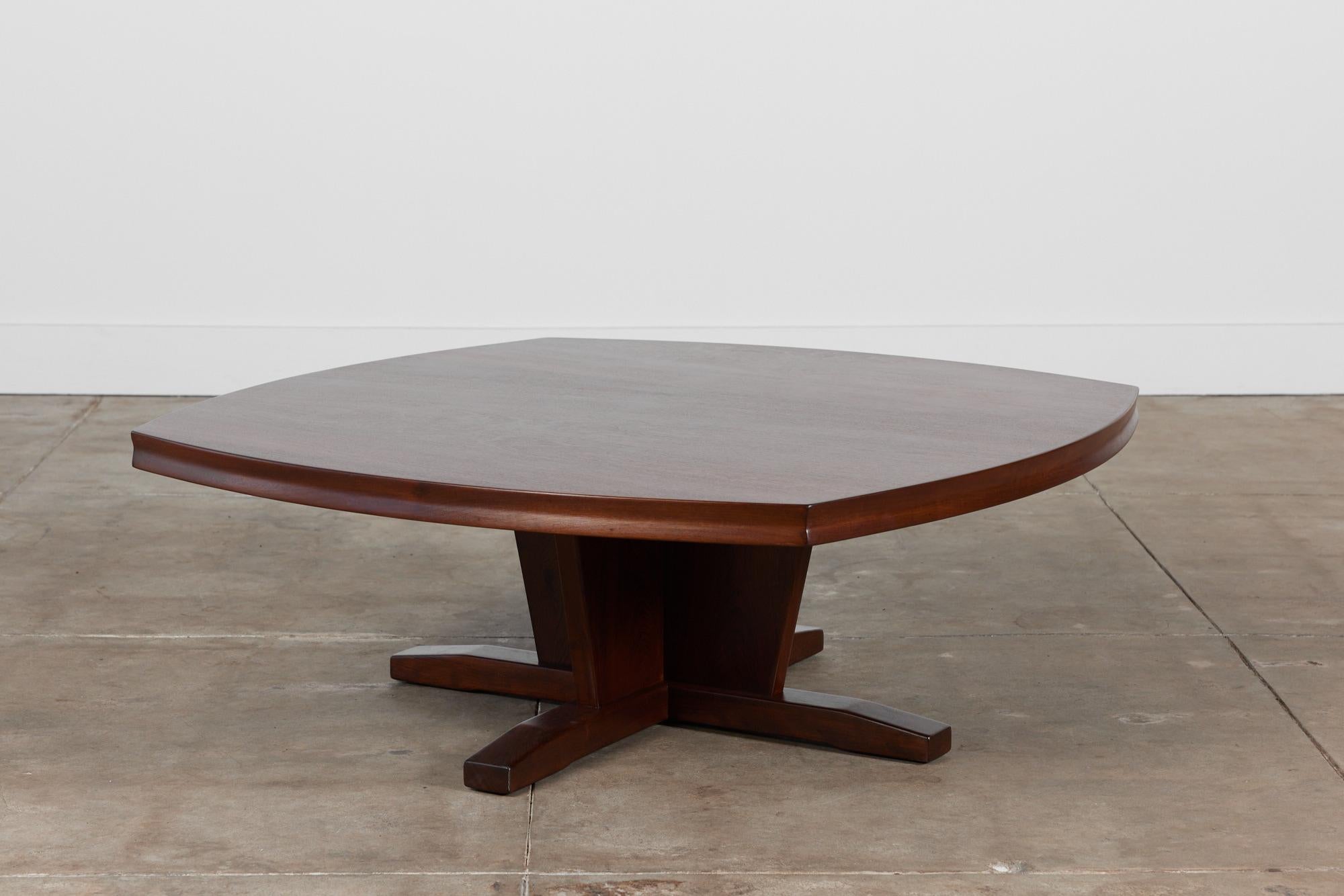 Coffee table in the style of acclaimed midcentury designer George Nakashima. This example is made of walnut and features a square table top with rounded sides. The table has a soft divot that extends around the outer rim of the table top. It is