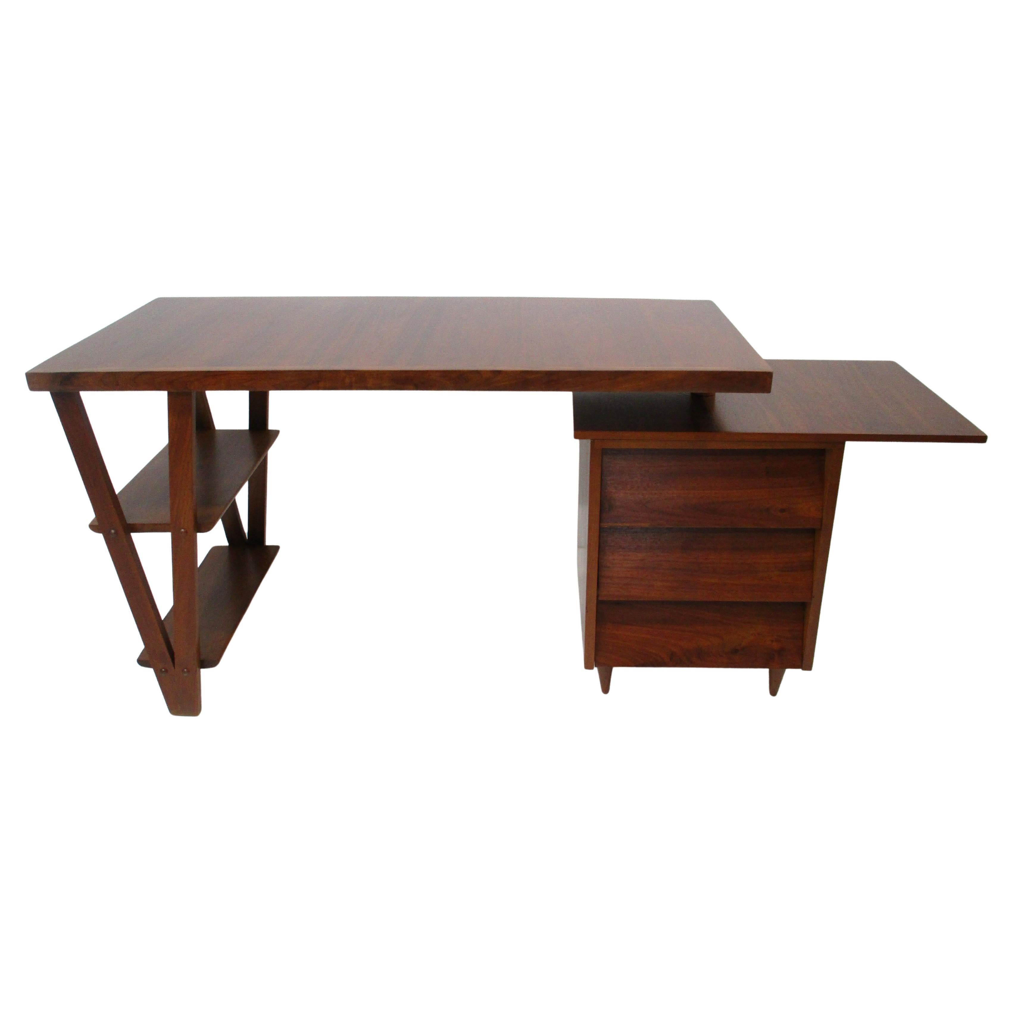 A well grained medium toned walnut desk which can swivel to any position and a swiveling small lower end platform for more work space. Three drawers having plenty of storage, and two shelves to the leg supports this functional desk can be used in