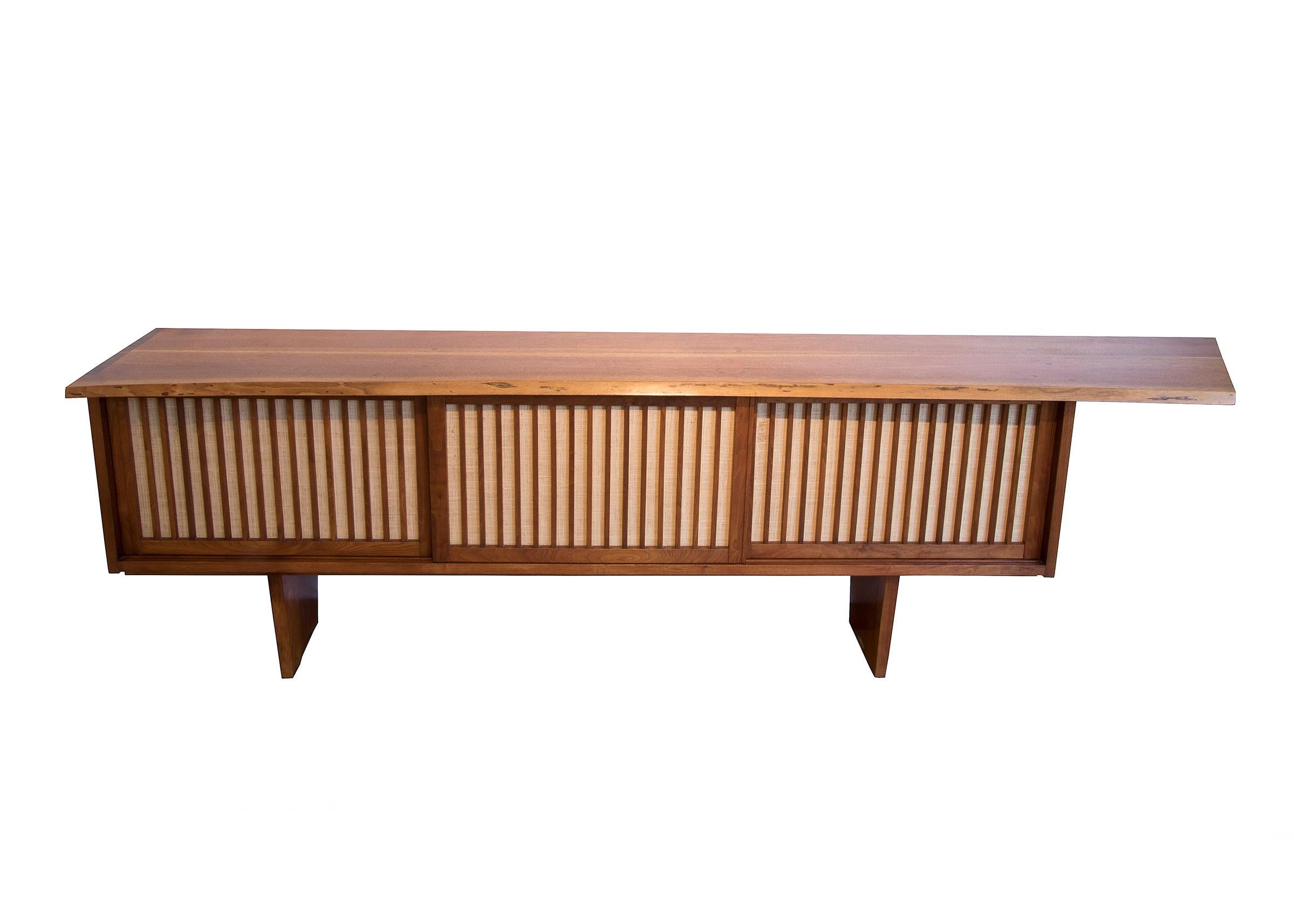 Rochlis Case by George Nakashima, 1966. This credenza (sideboard) is crafted from American Black Walnut and Pandanus (grass cloth) with an overhang and three sliding doors with inside drawers and storage spaces. Concise dovetail wood-joints bond the