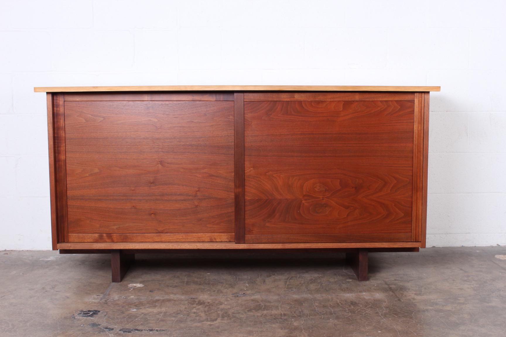 A walnut sliding door cabinet with free-edge sap grain top and overhanging sides. Made by George Nakashima in 1962. Sold with a copy of the original order card.