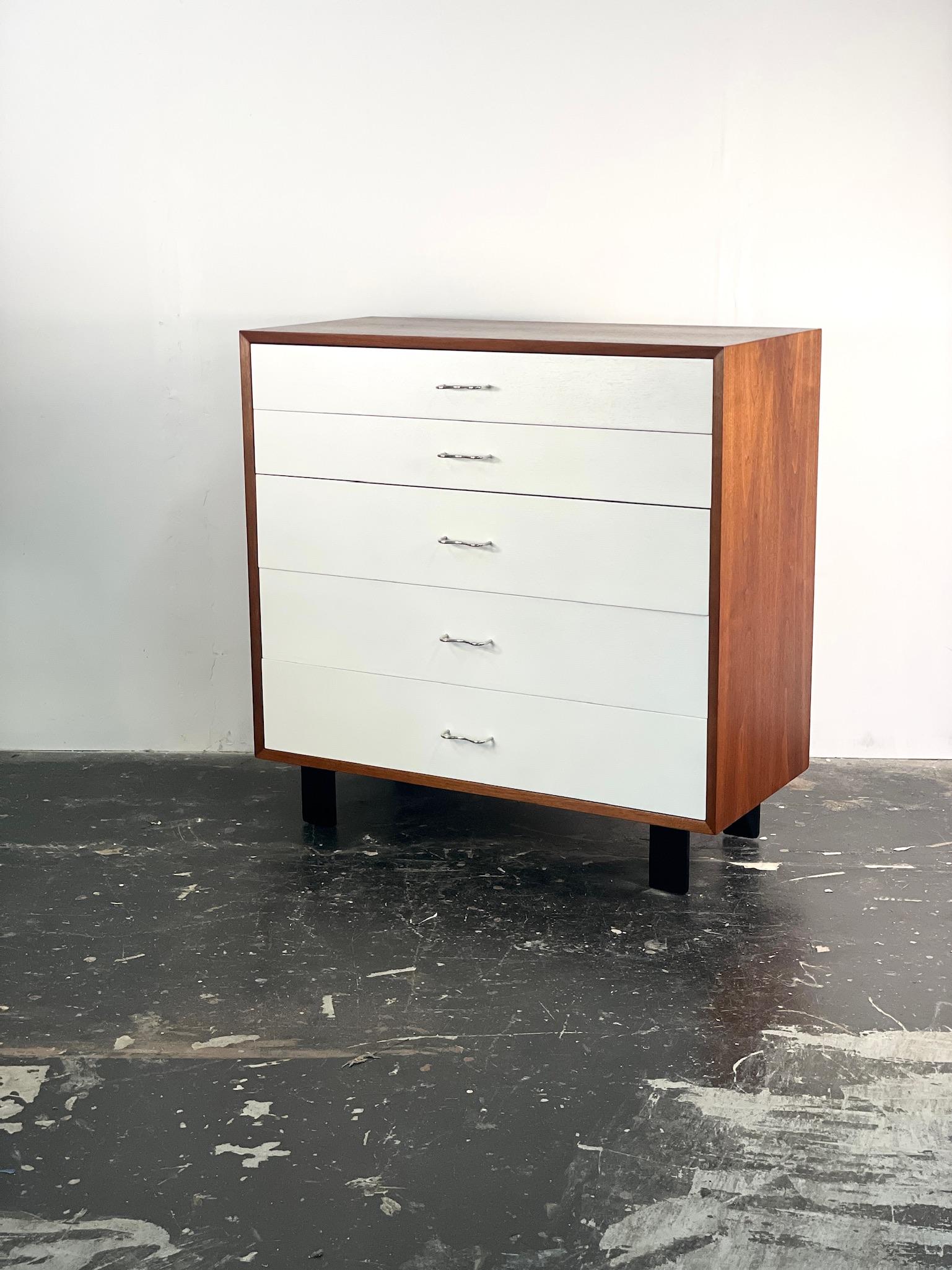 Bellissima cassettiera in bianco e noce di George Nelson per Herman Miller. Questo comò appartiene alla serie Basic con le sue iconiche gambe in legno laccato nero, la bellissima cassa in noce e le originali maniglie in argento che conferiscono a