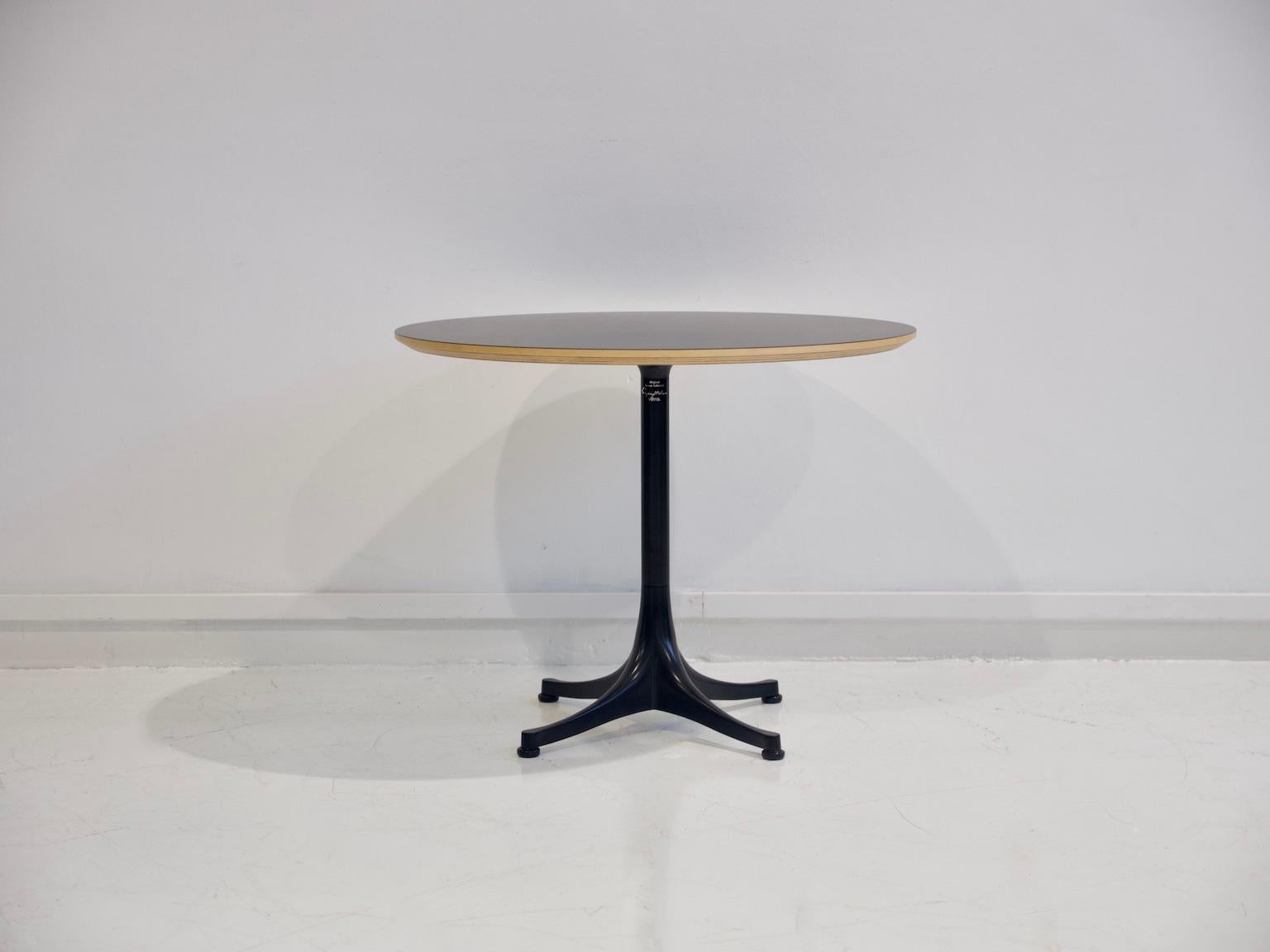 Guéridon, conçu à l'origine par George Nelson en 1954, avec une base à quatre branches en aluminium laqué noir. Plateau de table en stratifié noir avec bord visible en placage de bouleau. Produit par Vitra.