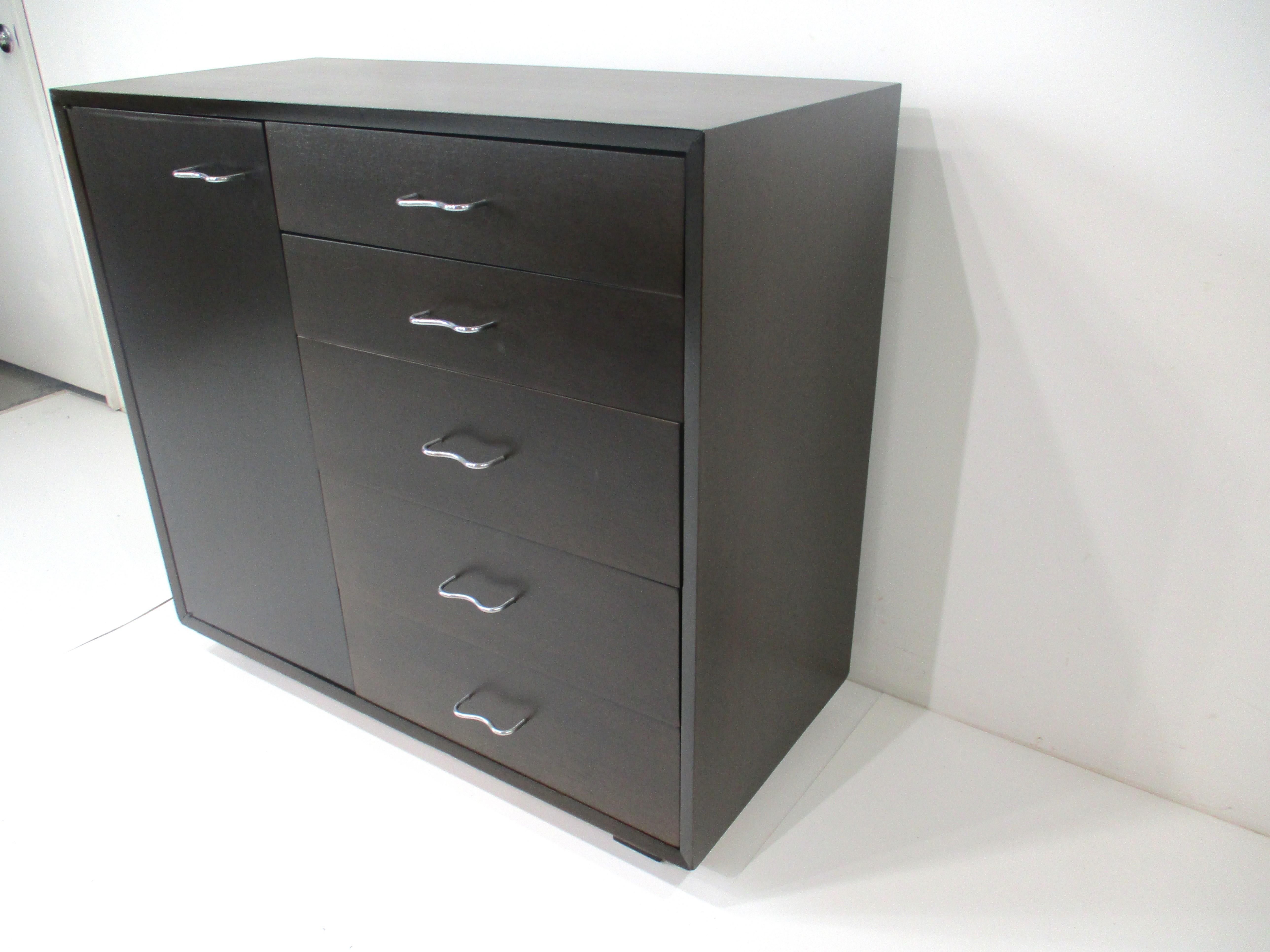 A very well crafted dresser chest or cabinet standing on shorter legs in a dark ebony finish with side door having two adjustable shelves . The other side has five drawers , all with sculptural stainless steel pulls and contrasting oak interior to