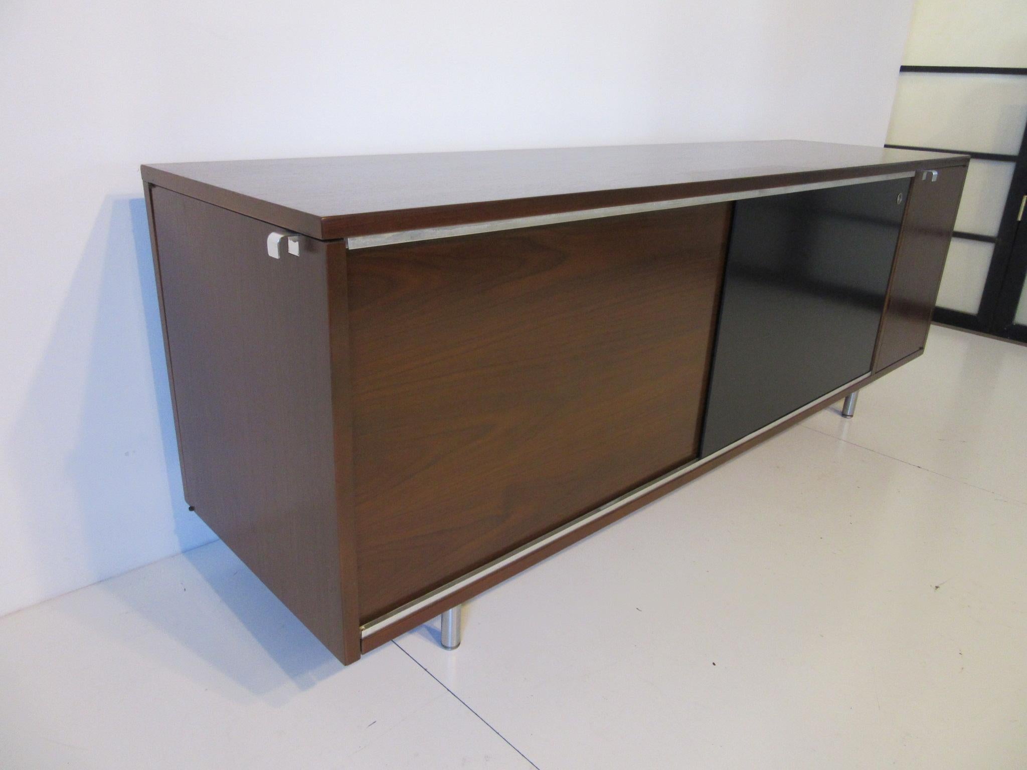 A walnut credenza with sliding door five drawers to the inside, small door to the right with a shelve and storage and a door on the end with the same. Complemented by brushed stainless legs, pulls and details. The backside is finished with the same