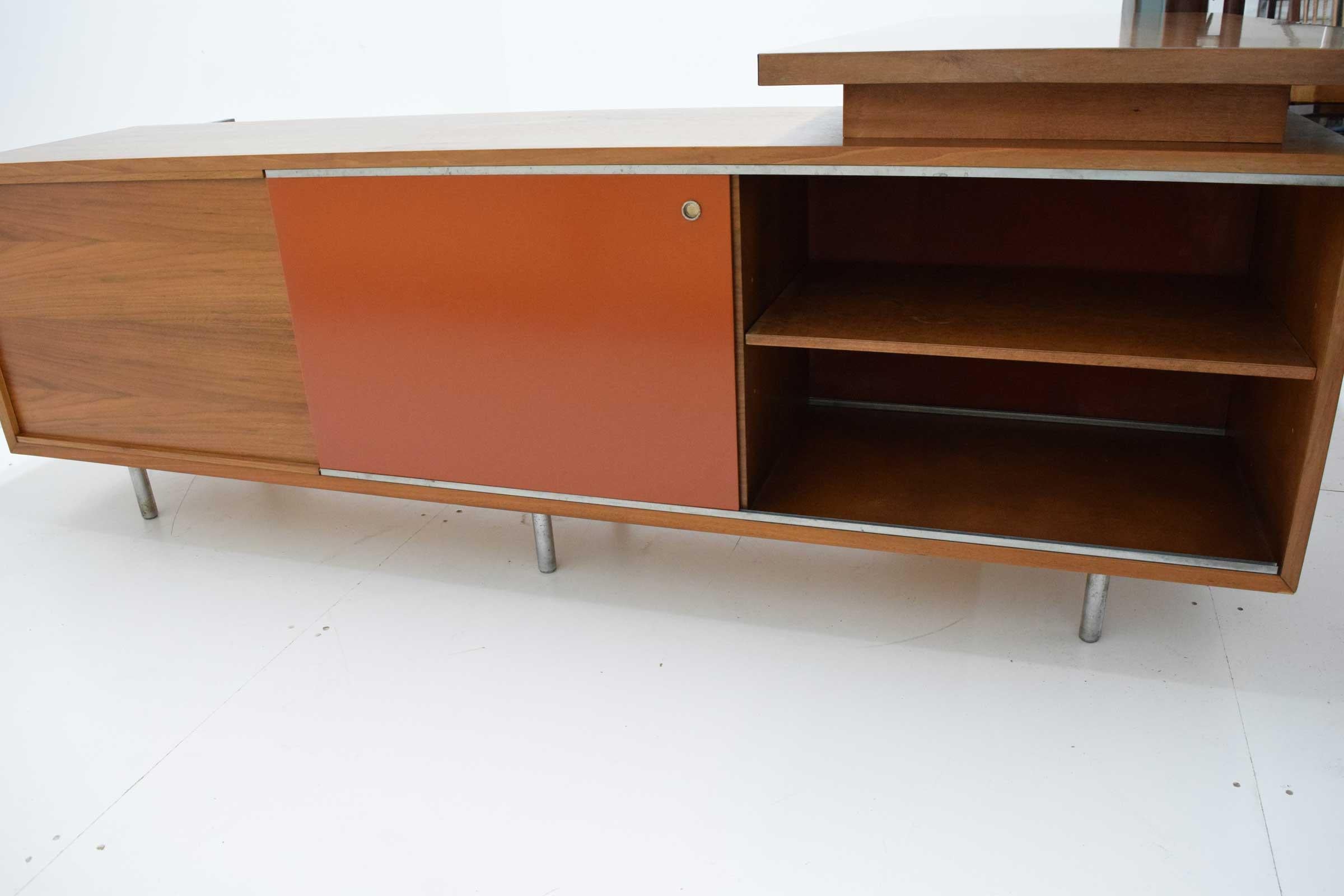 Executive L-shaped desk with original wood grained laminate writing surface, two sided credenza with red masonite sliding doors, drawers and adjustable shelves. Walnut on nickel plated steel legs. Cane modesty panel.
Work surface 78