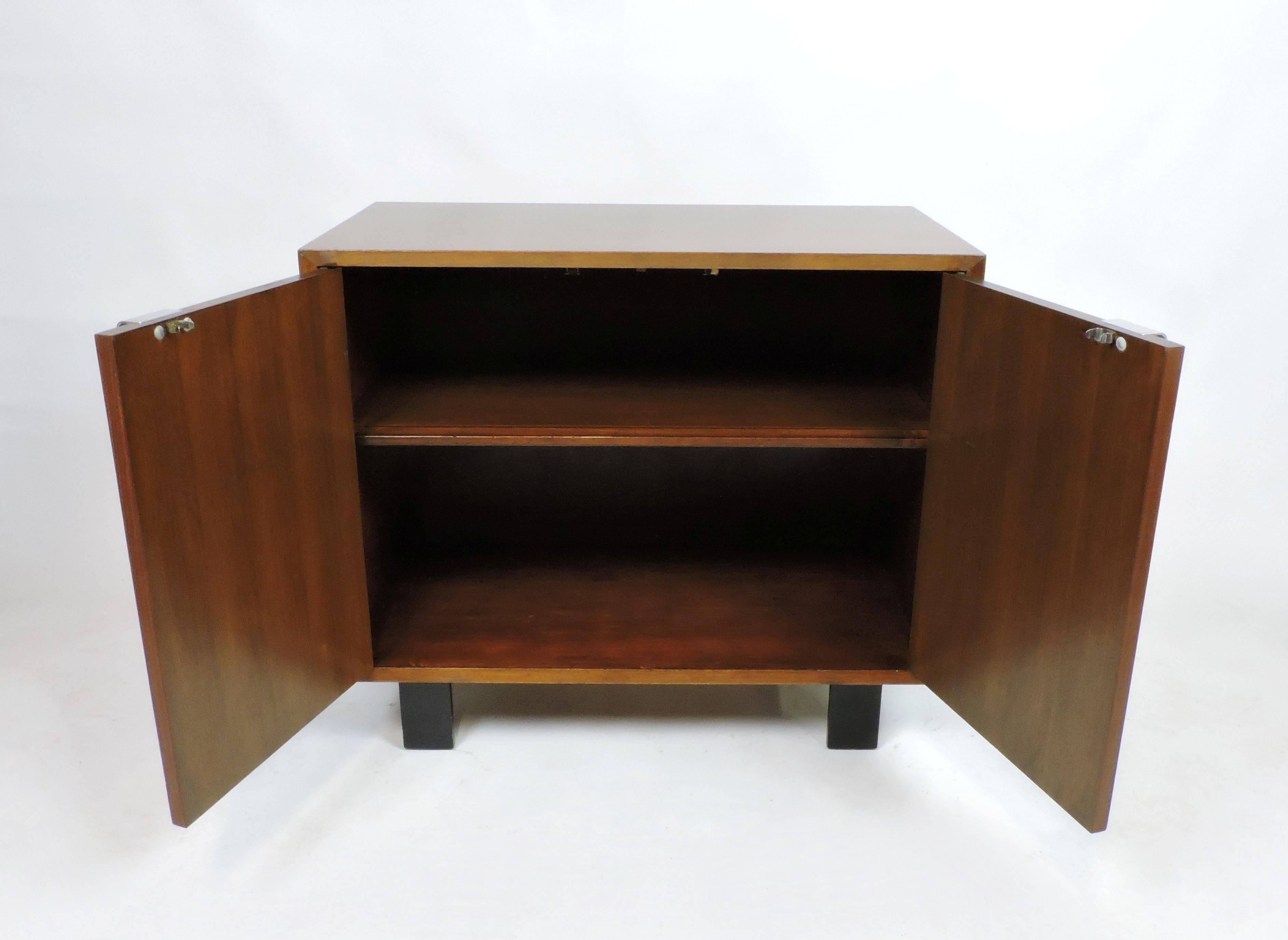 Handsome and distinctive walnut cabinet designed by George Nelson and manufactured by Herman Miller. Part of the Basic Cabinet Series, this cabinet has two doors and an interior adjustable shelf. Classic J shaped metal pulls and black block feet