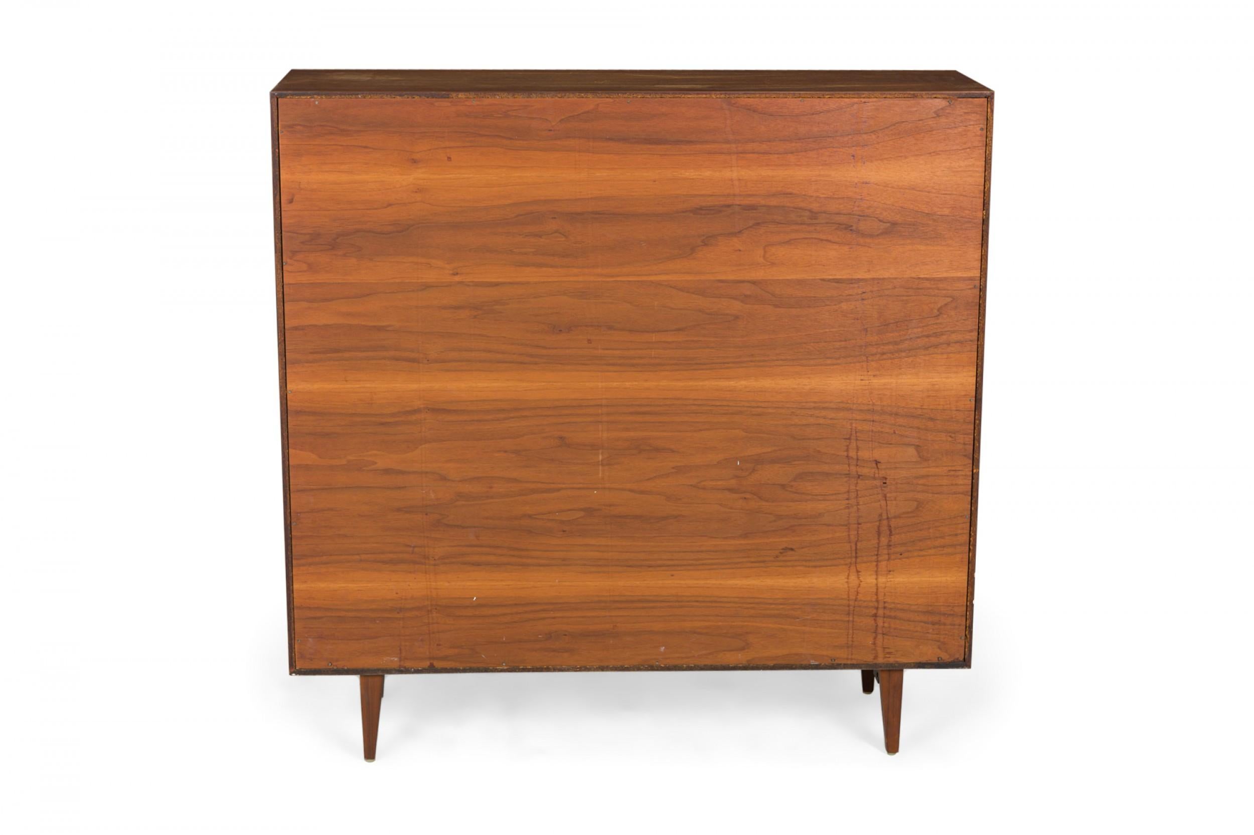 American Mid-Century walnut veneer bookcase with two shelves in a rectangular cabinet, resting on four tapered wooden legs. (BCS BASICS CABINET SERIES, GEORGE NELSON FOR HERMAN MILLER)

Condition: Good; Wear consistent with age and use