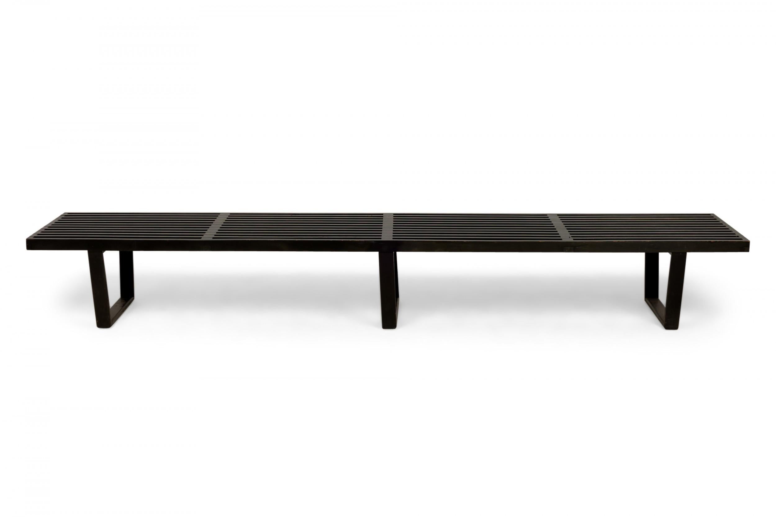 Panca a piattaforma rettangolare allungata del Mid-Century americano con seduta a doghe verniciata di nero sostenuta da tre gambe trapezoidali in metallo nero. (GEORGE NELSON PER HERMAN MILLER)

Condit: Buono; Usura coerente con l'età e l'utilizzo