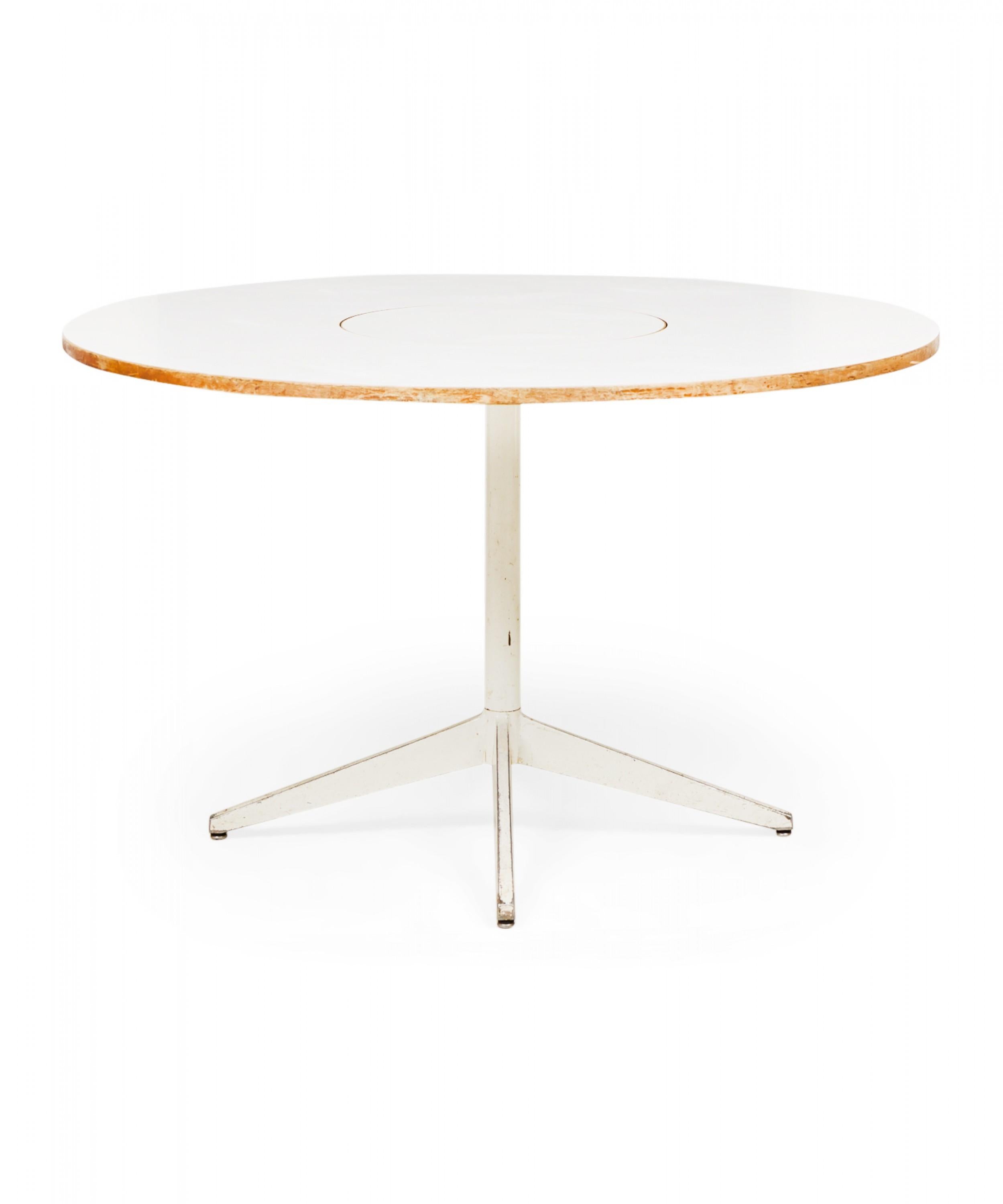 American Mid-Century circular dining table with a white laminate top featuring a central lazy susan circular section that rotates, resting on a white powder coated metal pedestal base with four angled legs. (GEORGE NELSON FOR HERMAN MILLER)